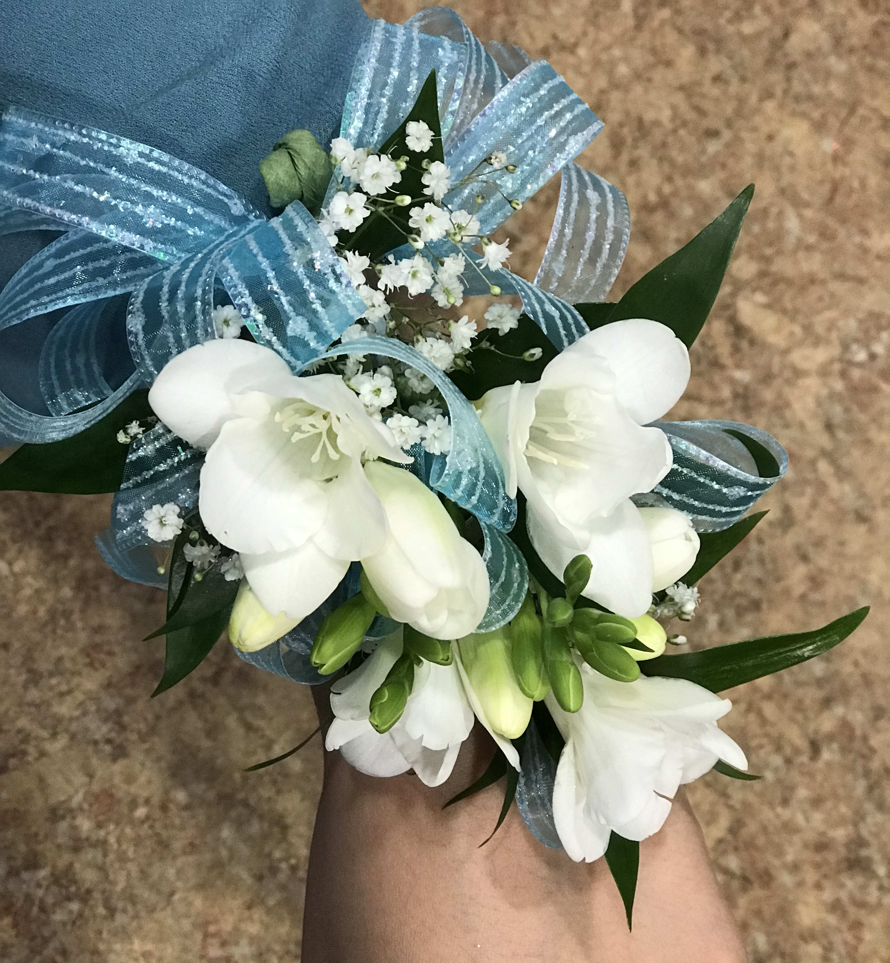 White floral wrist corsage with blue ribbon and baby's breath