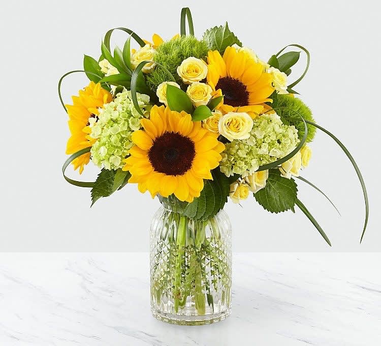Rise and Shine  - This arrangement is sure to brighten the day! Bright yellows usher in cheeriness and smiles. Sunflowers, green hydrangea, bear grass and spray roses are featured in this bouquet. 