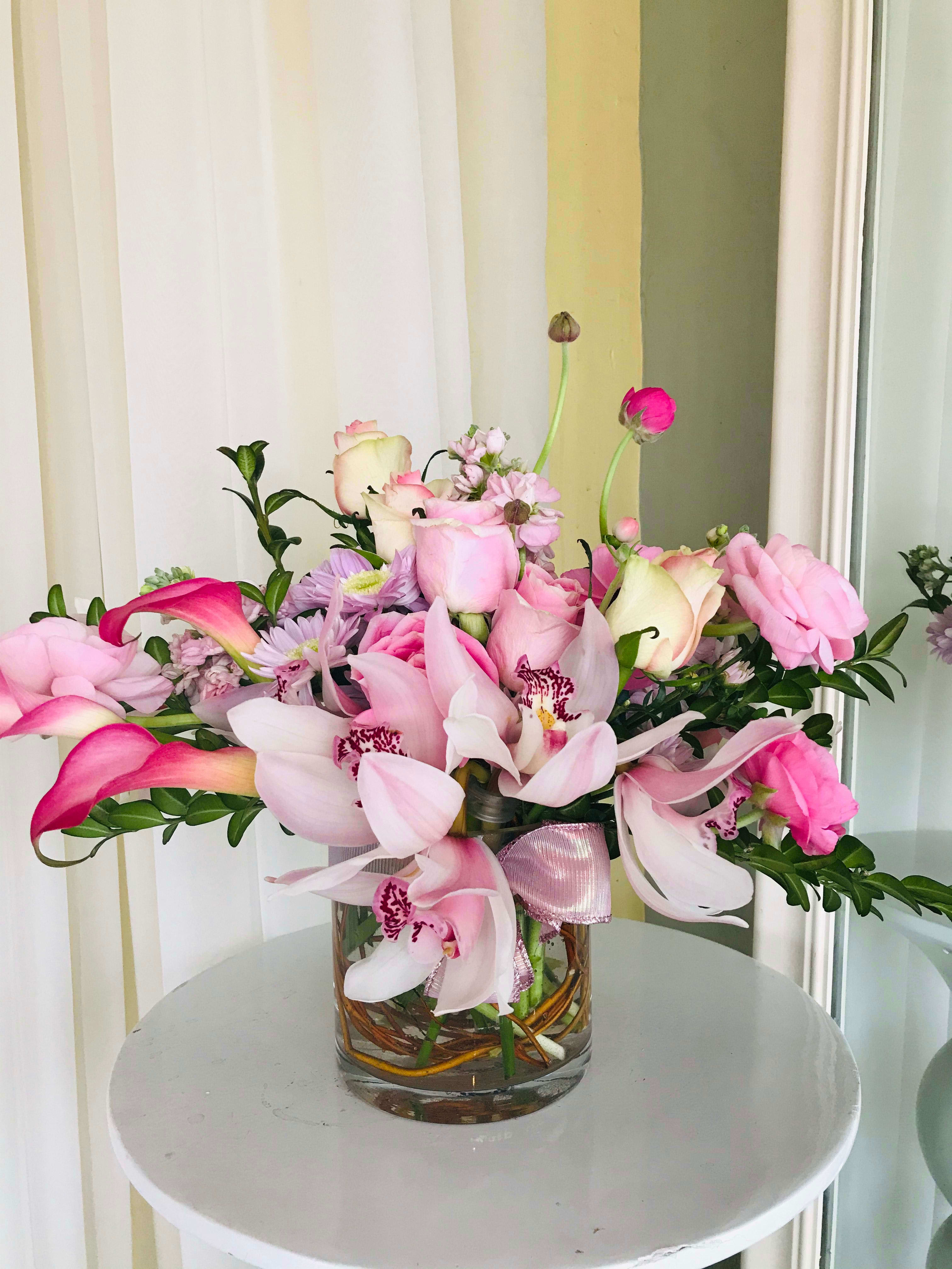 Pink and white flowers arranged in a glass vase with a ribbon