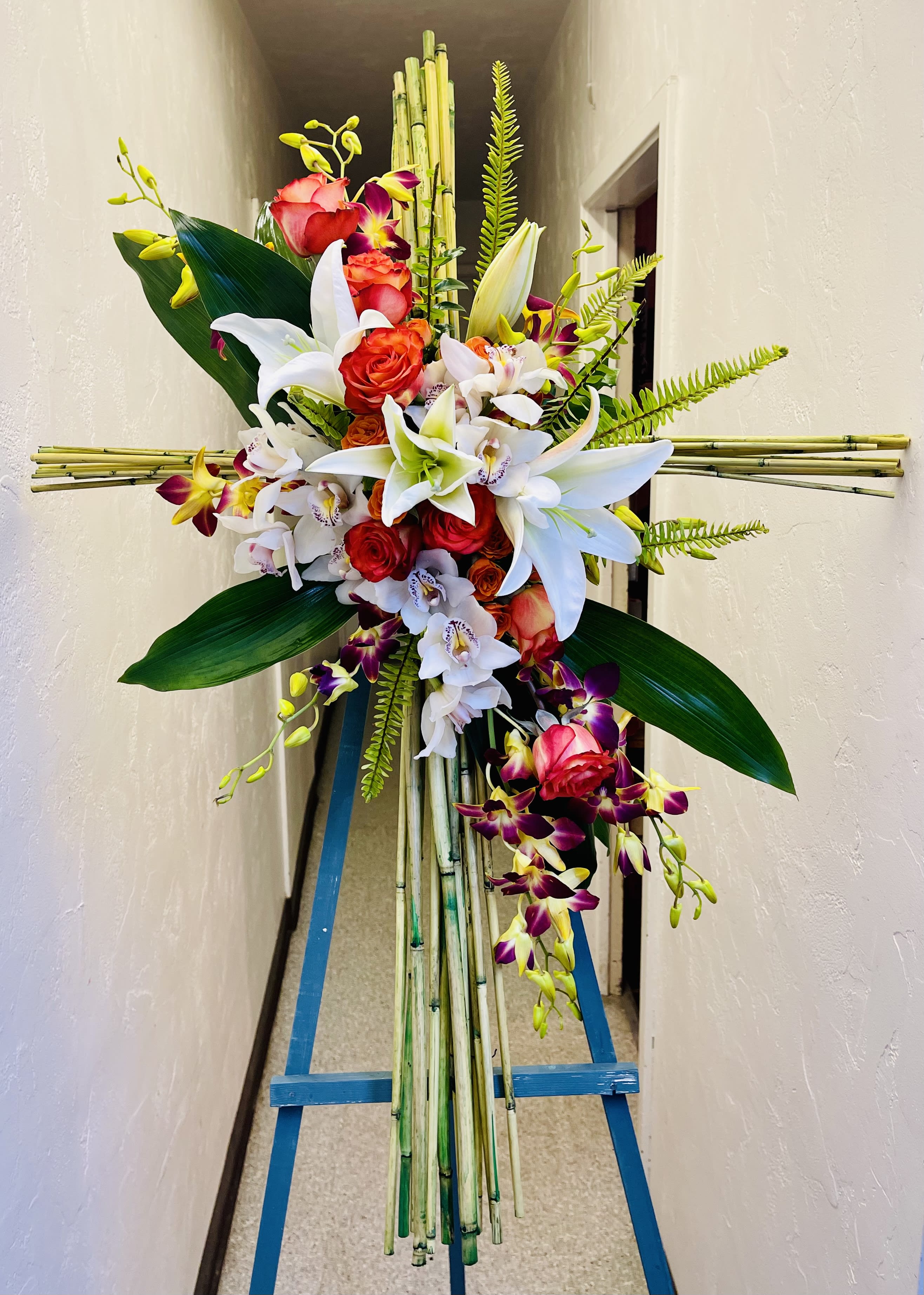 Tall floral standing spray with red roses, white lilies, and orchids on bamboo