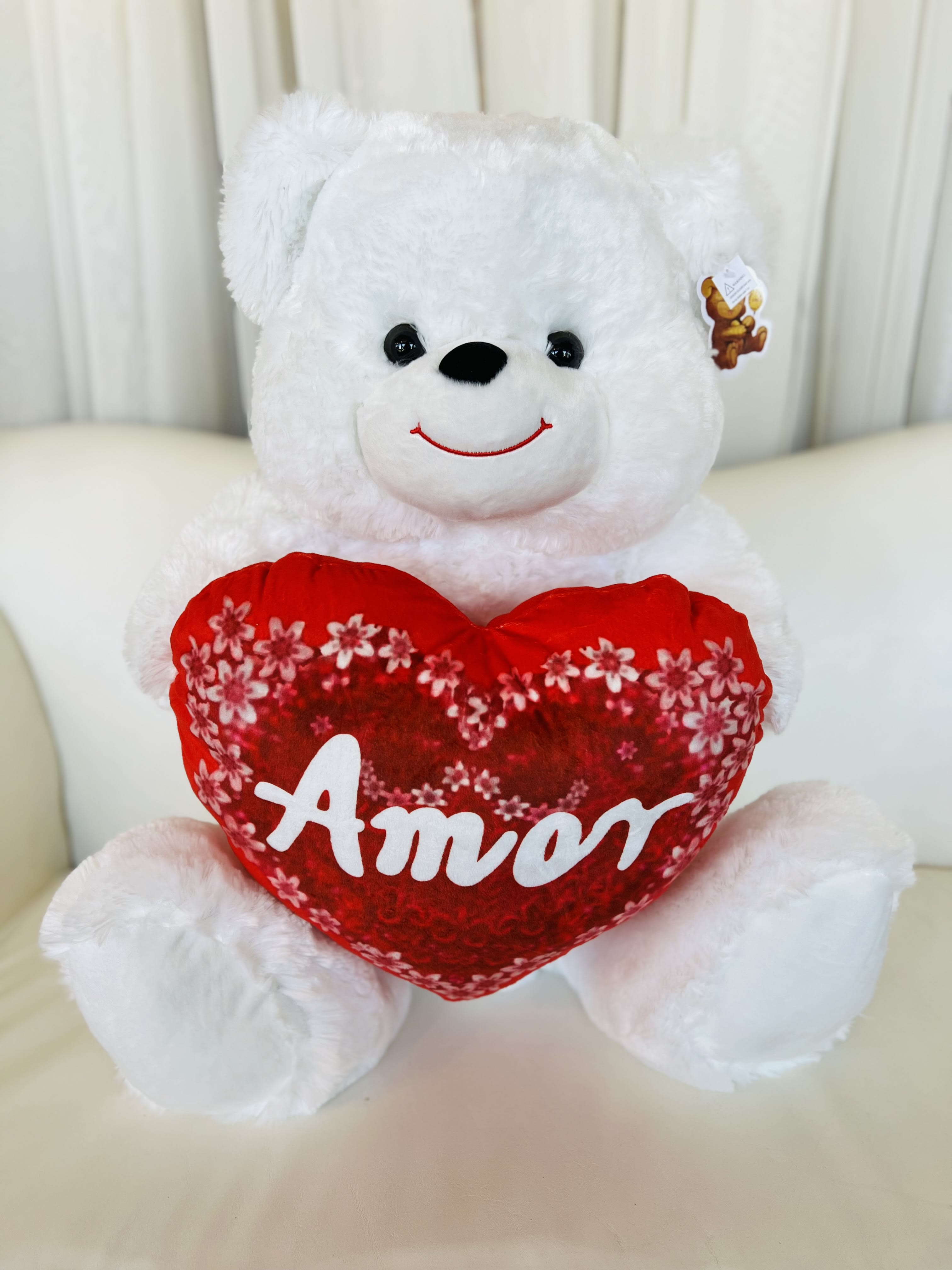 White teddy bear holding a red heart pillow with the word Amor