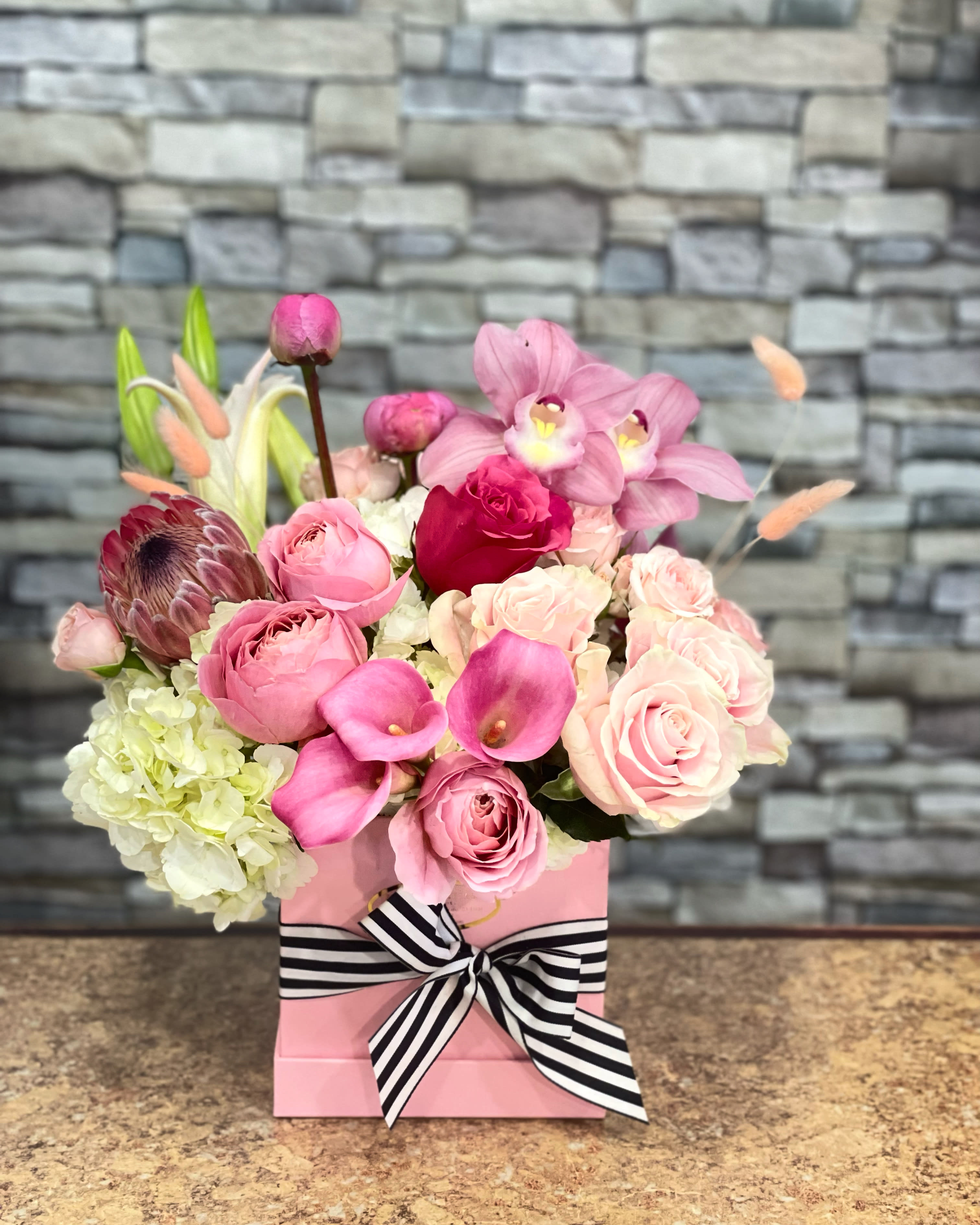 Pink floral arrangement in a pink box with a striped ribbon