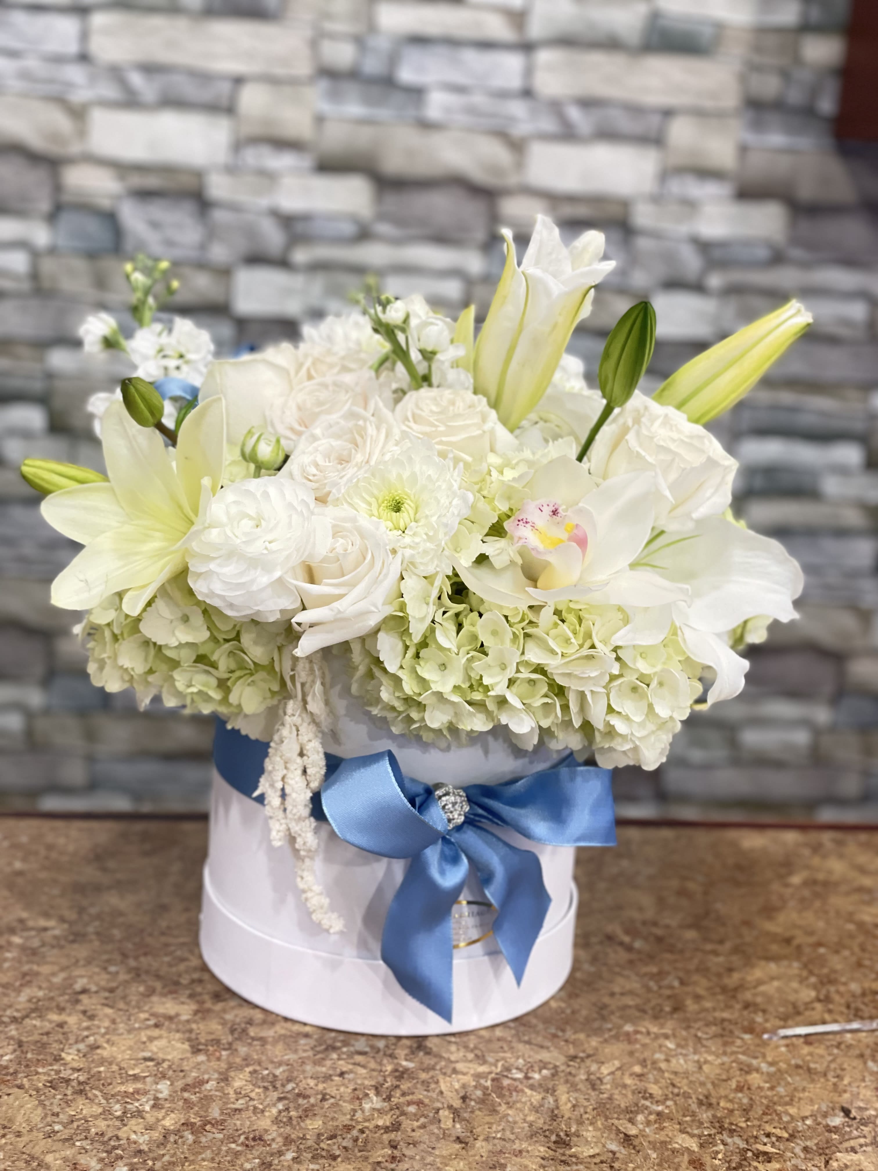 White floral arrangement in a round box with a blue ribbon