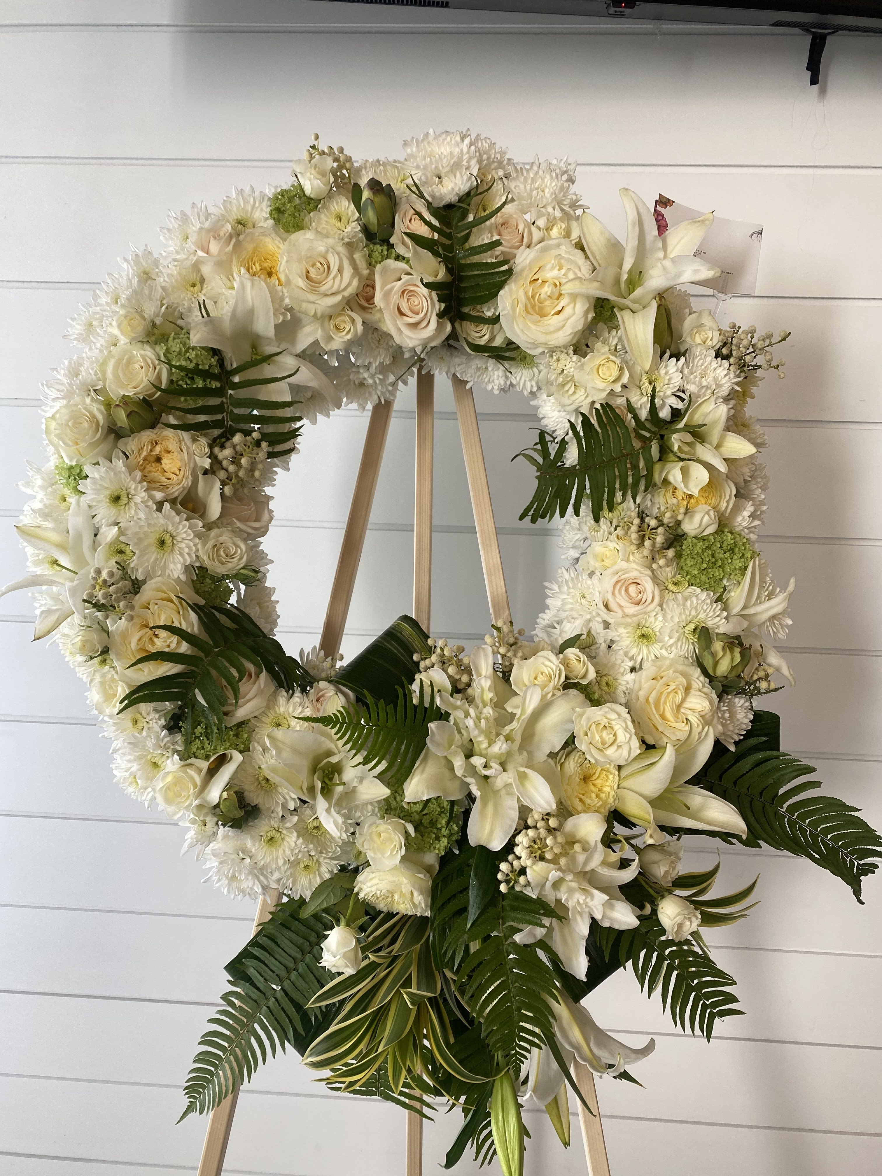 White floral wreath on a wooden easel with roses and lilies