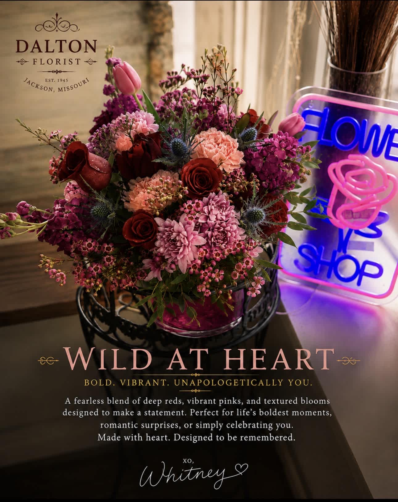 Mixed bouquet of pink and red flowers in a vase beside a neon flower shop sign