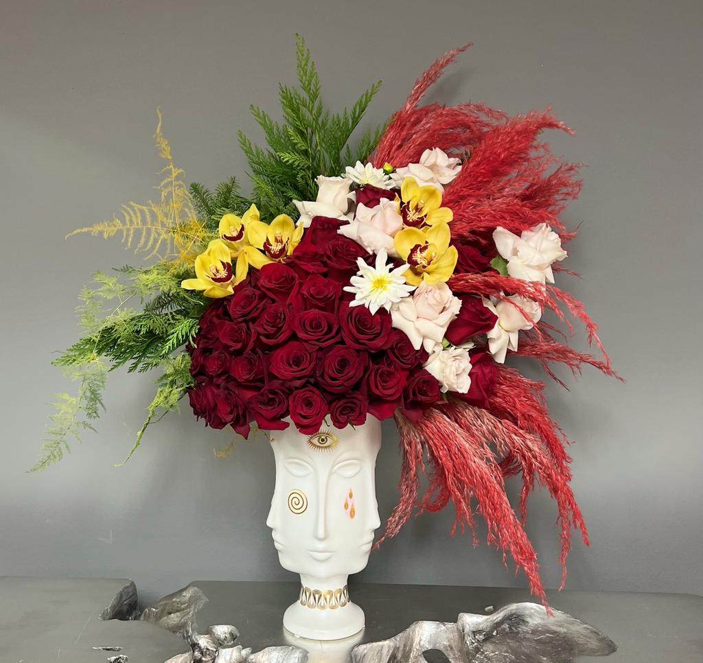 Large floral arrangement in a white sculptural vase with red, yellow, and white blooms