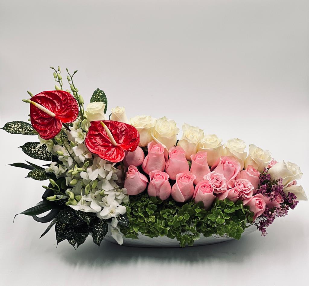 Pink and white roses with red anthuriums in a low white bowl