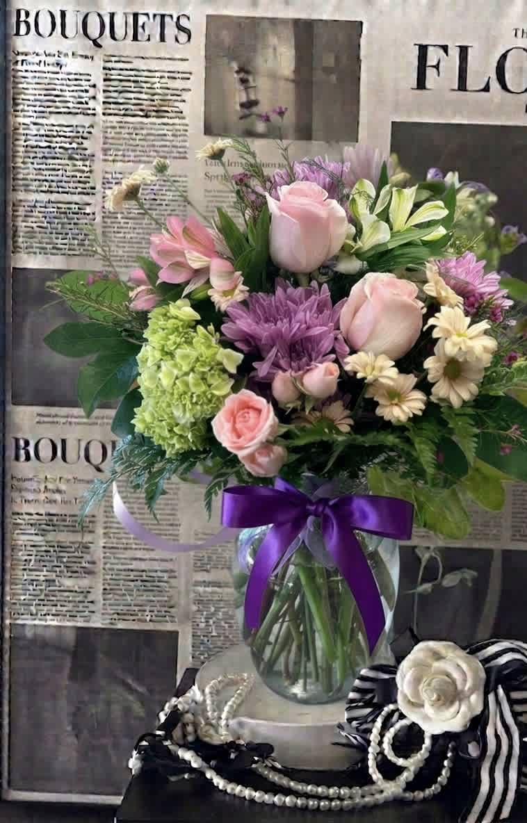 Mixed pink and purple bouquet in a glass vase with a purple ribbon