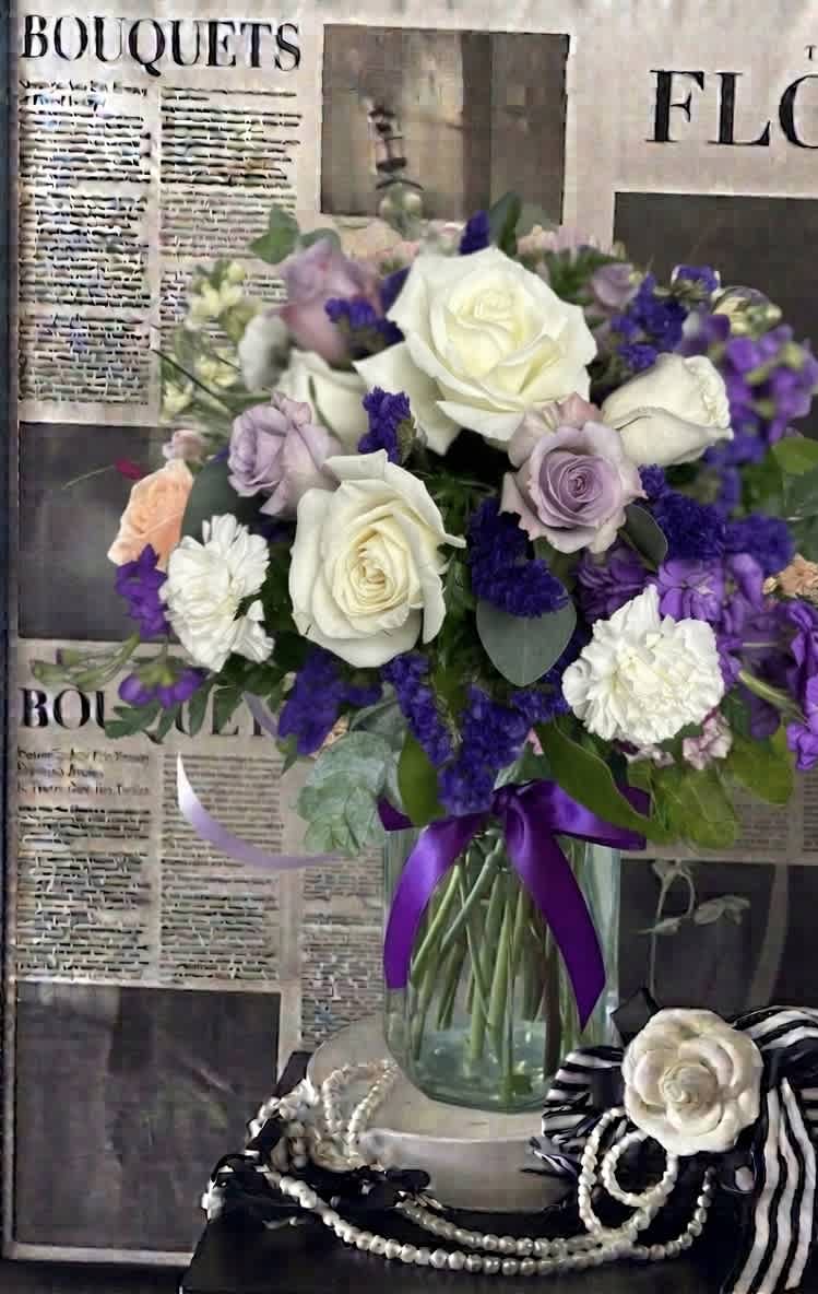 Bouquet of white, lavender, and purple roses in a glass vase with a purple ribbon