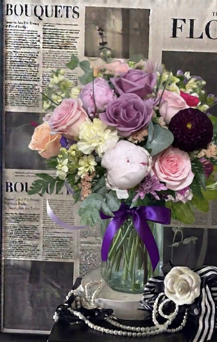 Mixed bouquet of pink, purple, and white flowers in a glass vase with a purple ribbon