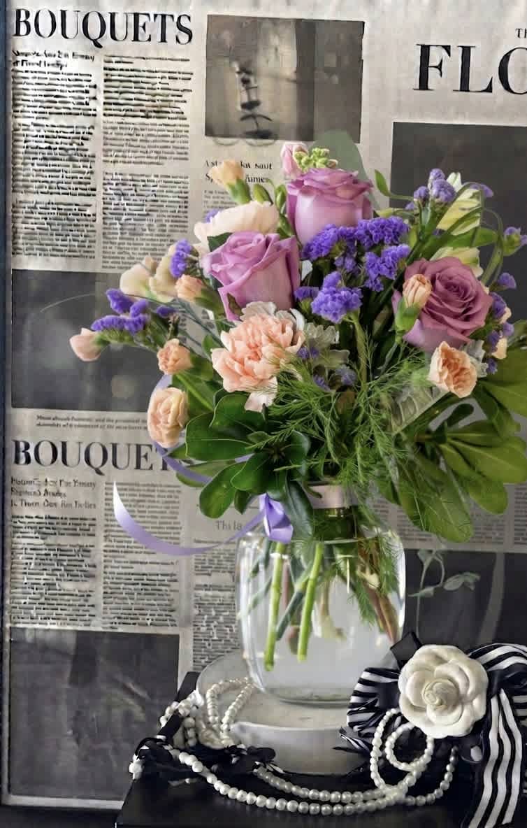 Bouquet of pink roses, peach carnations, and purple filler flowers in a glass vase
