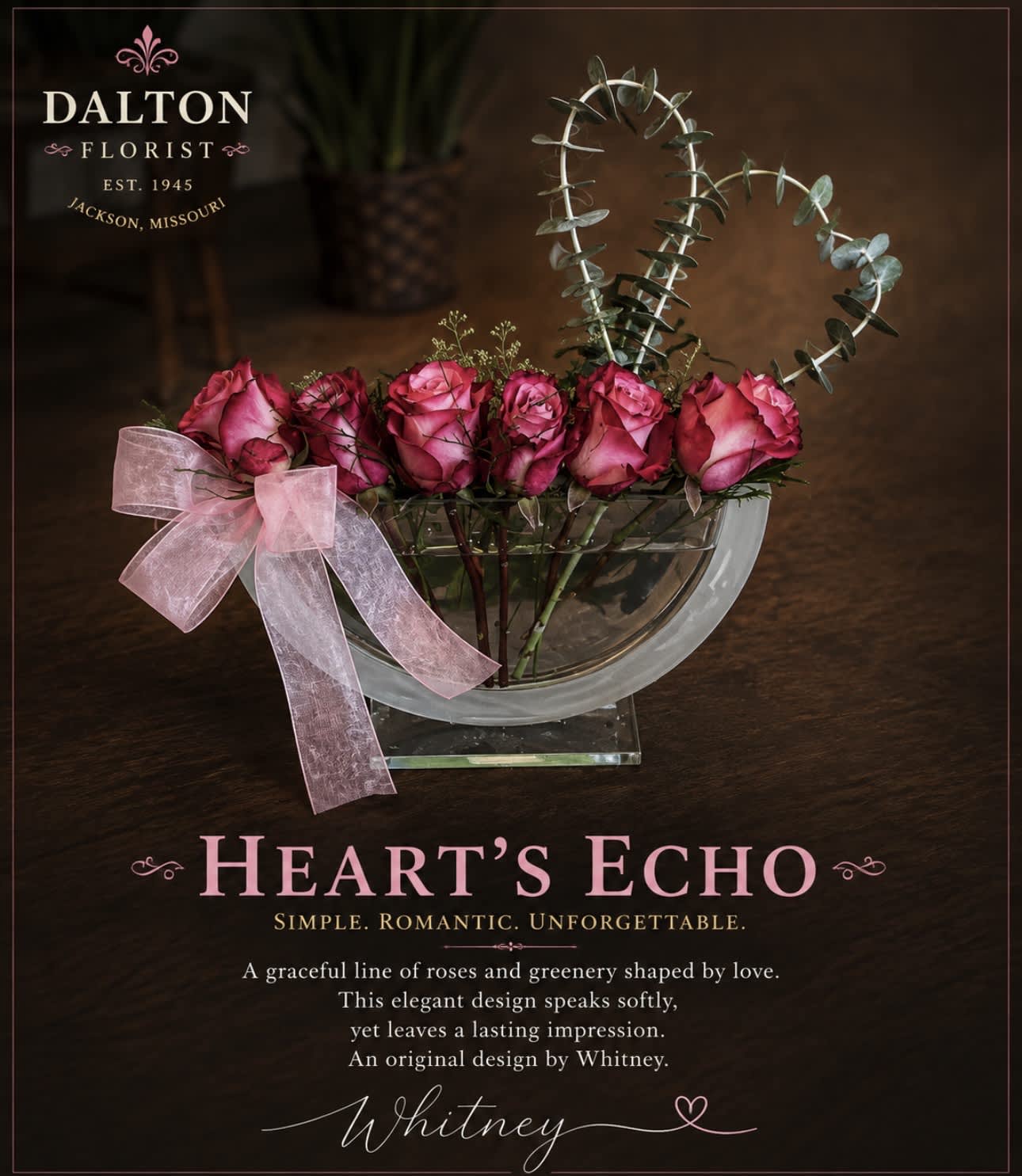 Pink roses in a clear bowl vase with a pink ribbon and heart-shaped eucalyptus