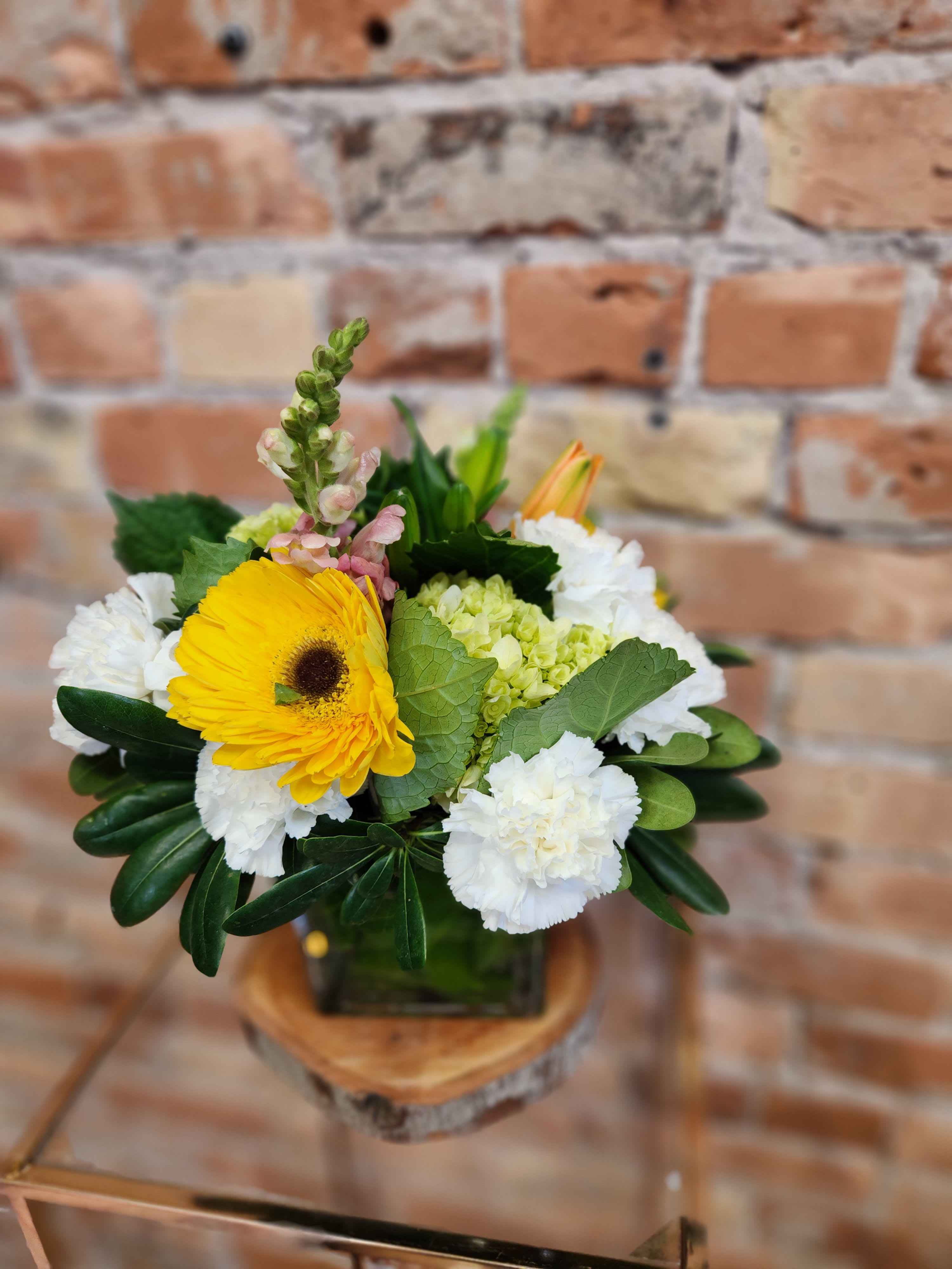 Bouquet of yellow gerbera daisies and white carnations in a glass vase