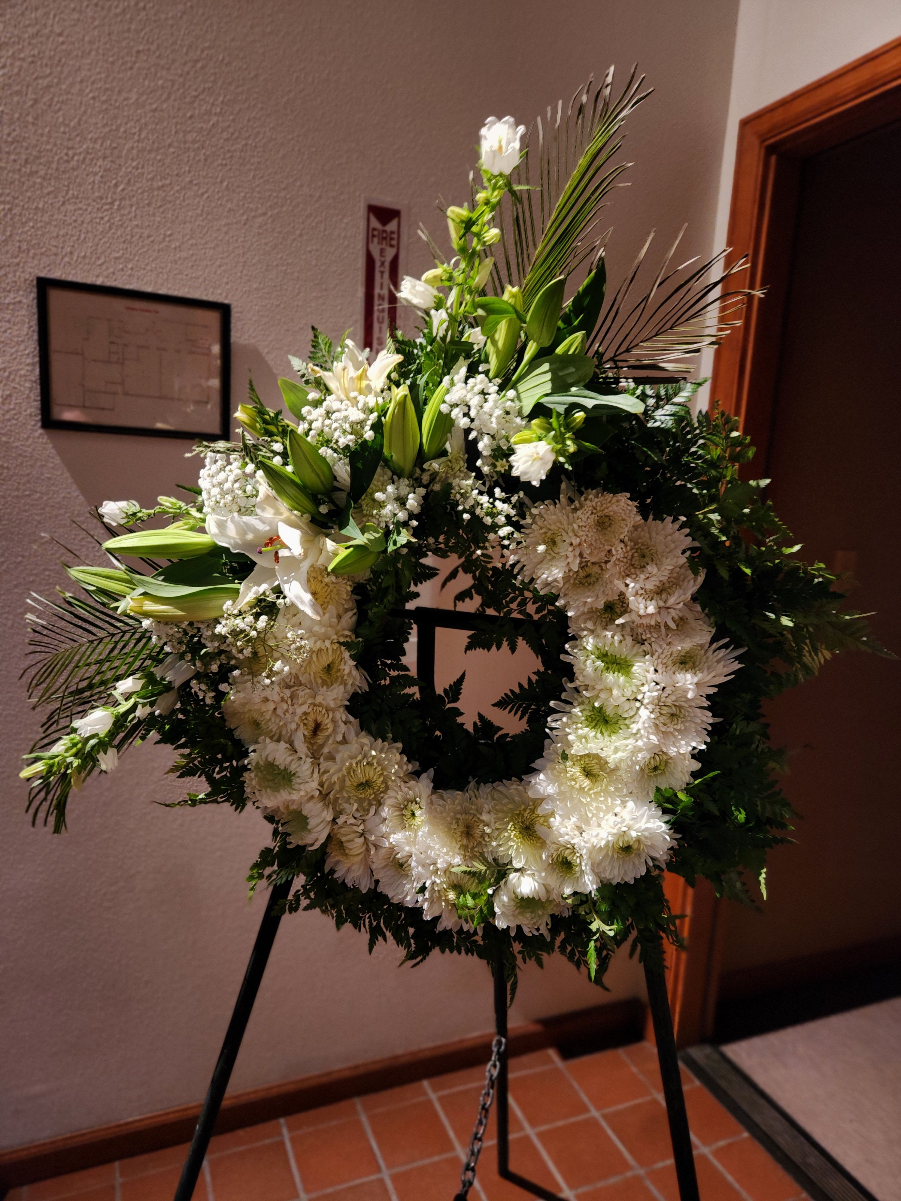 White floral wreath on a black easel with lilies and daisies