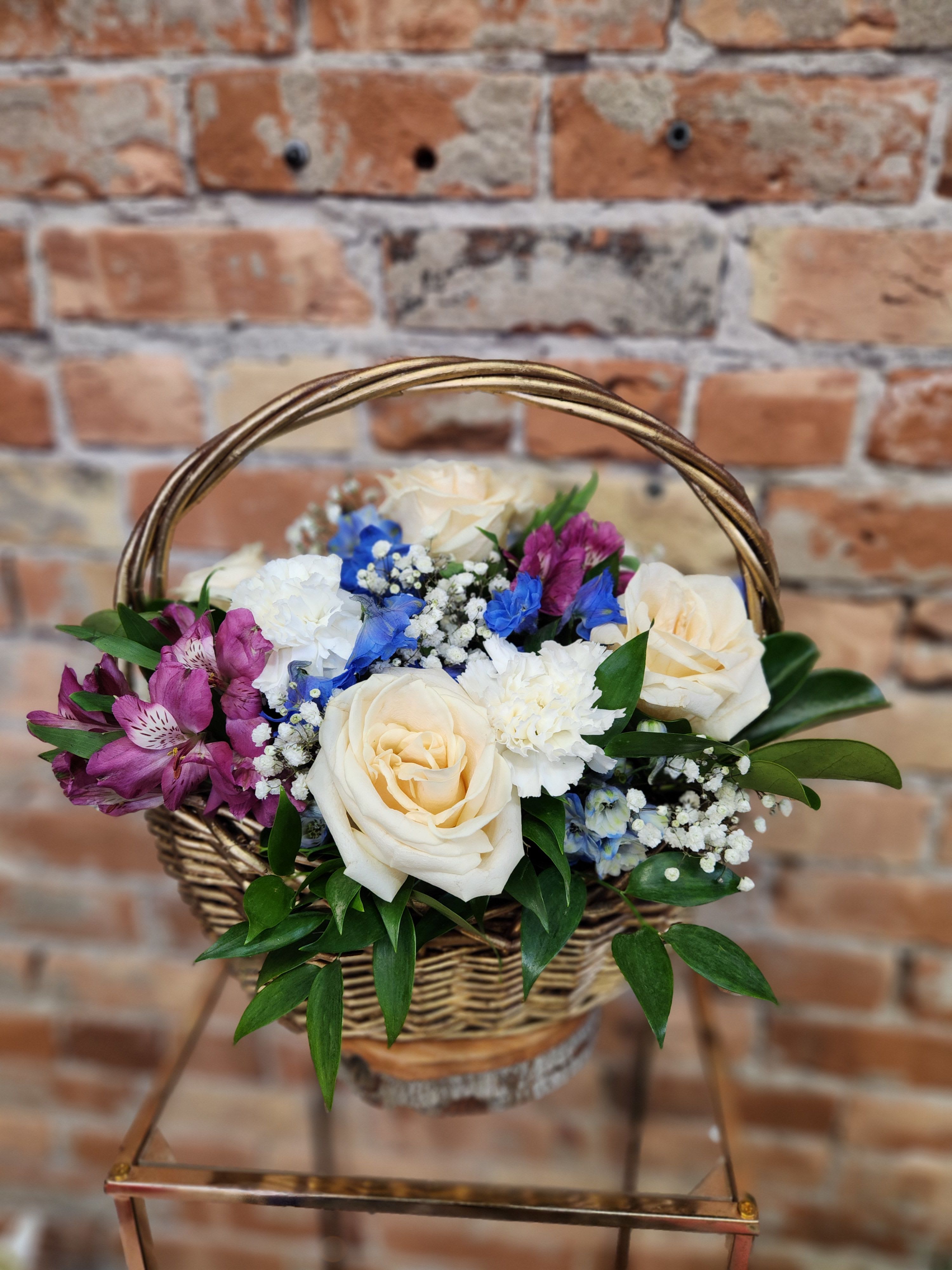 Basket arrangement with cream roses, purple blooms, and blue flowers