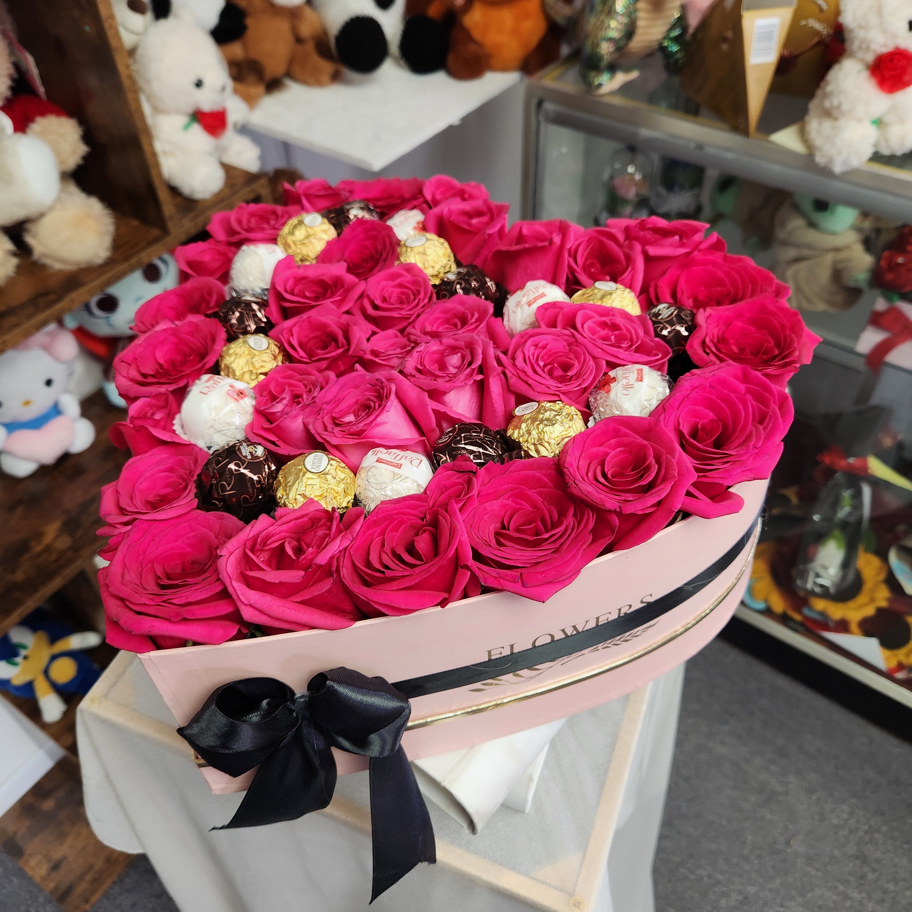 Heart-shaped box of hot pink roses with assorted chocolates and a black ribbon