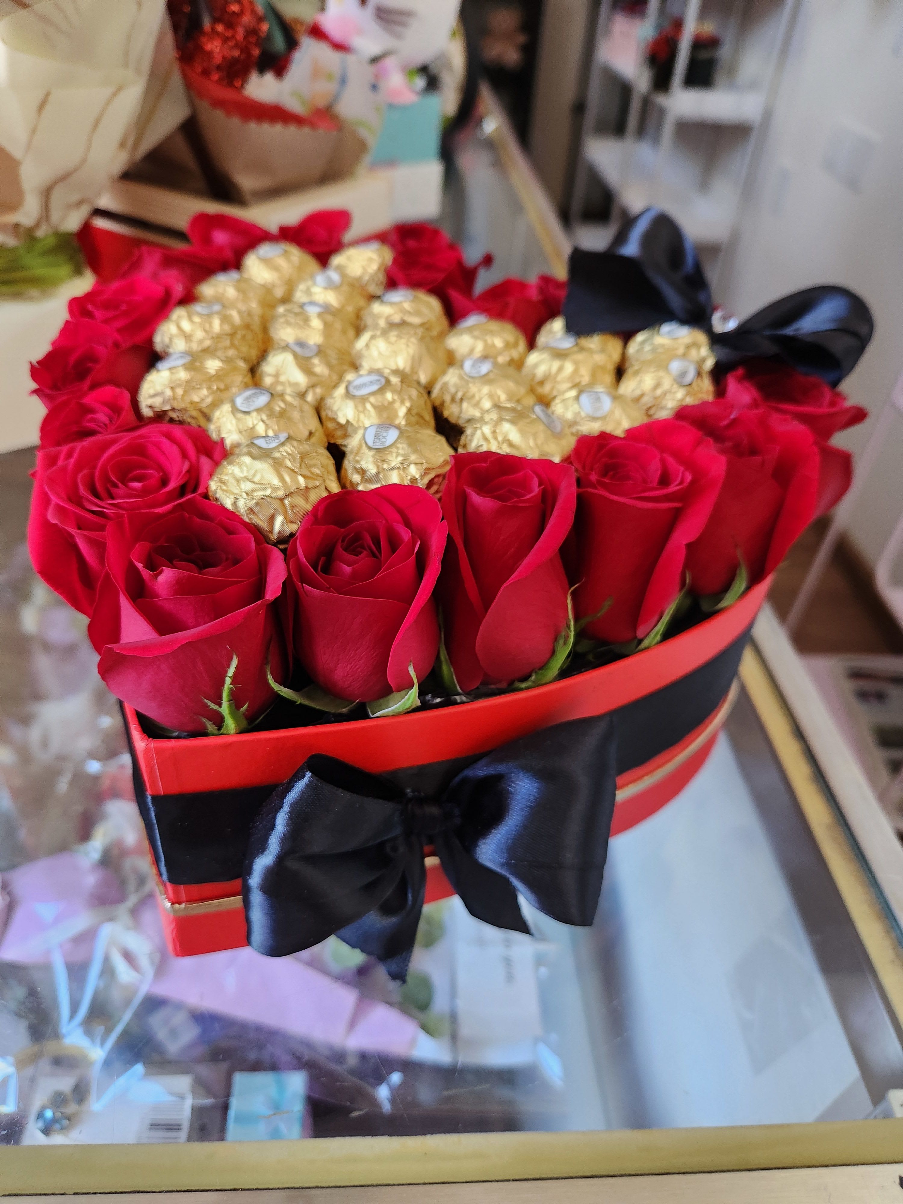 Heart-shaped box of red roses and gold-wrapped chocolates with a black ribbon