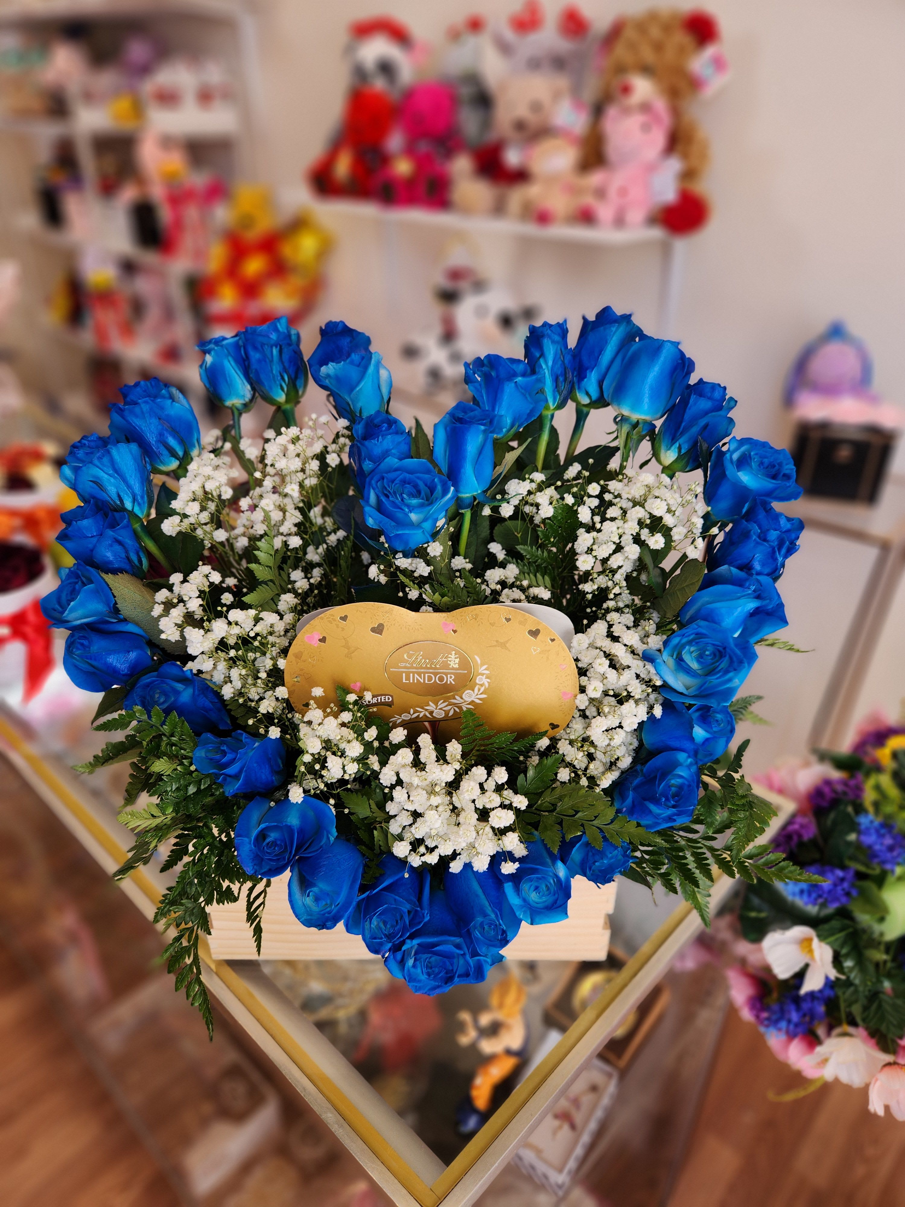 Blue roses arranged around a gold Lindor chocolate box
