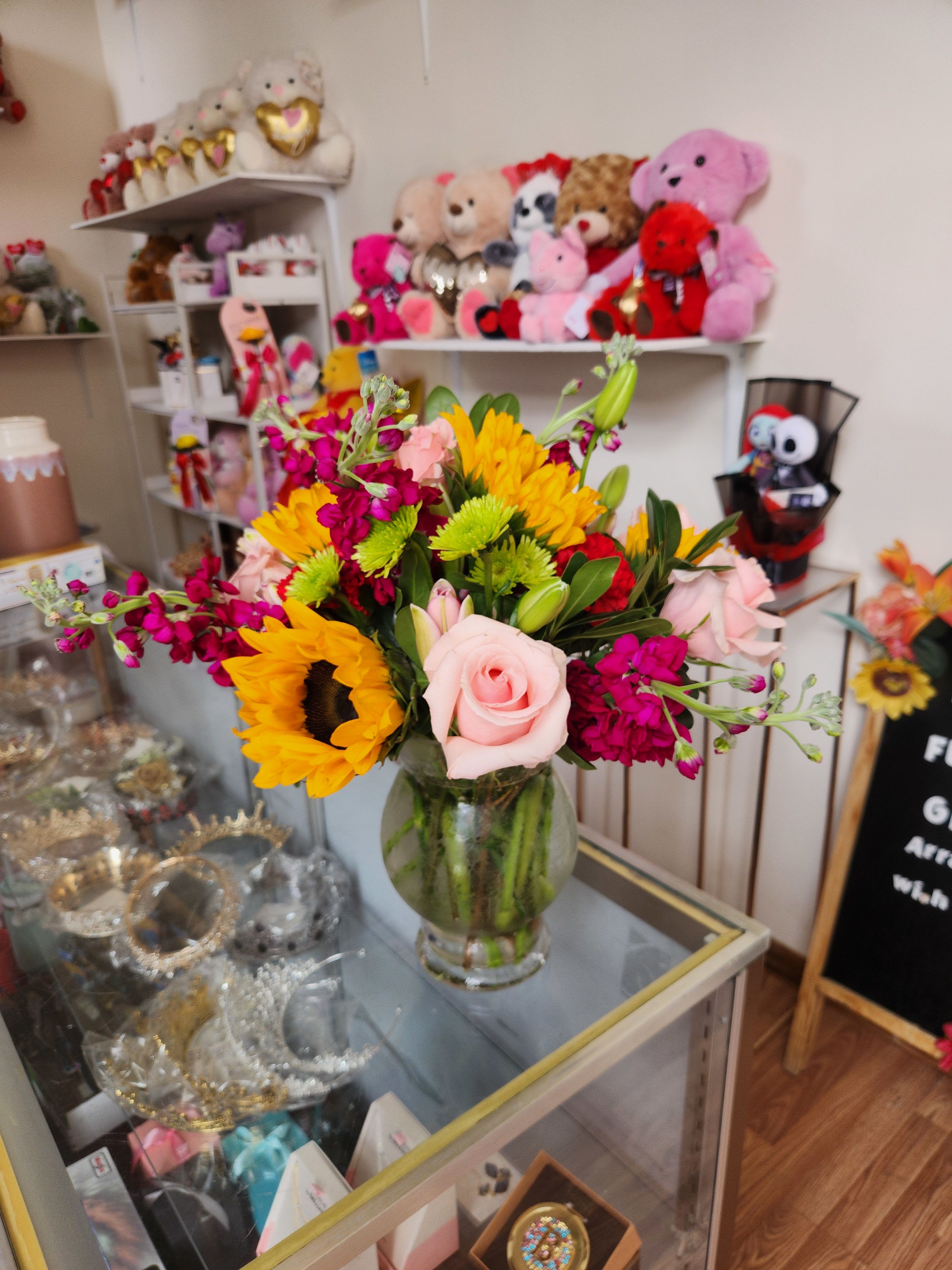 Mixed bouquet with sunflowers, pink roses, and magenta blooms in a glass vase