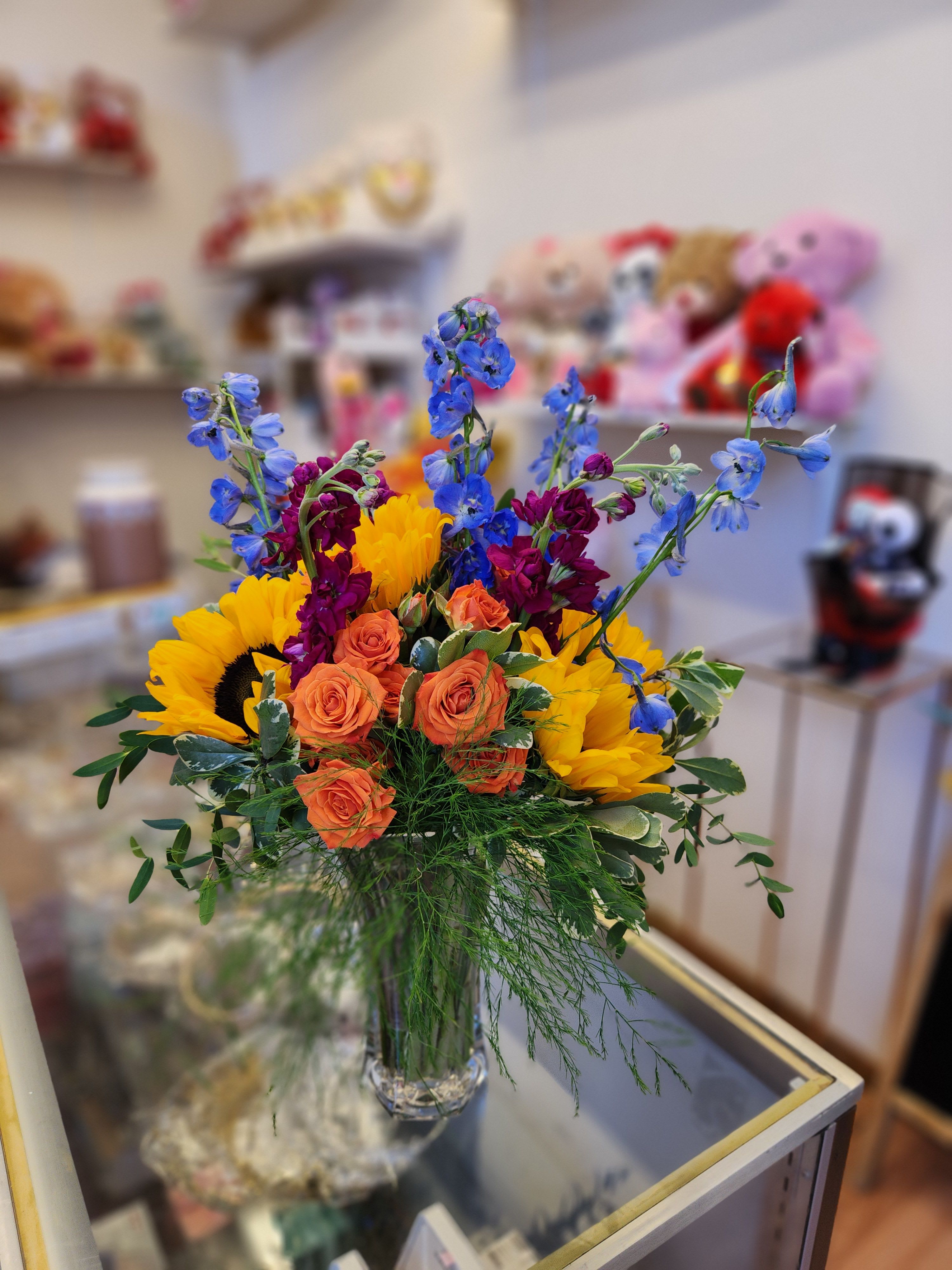 Bouquet of sunflowers, orange roses, and blue delphinium in a glass vase