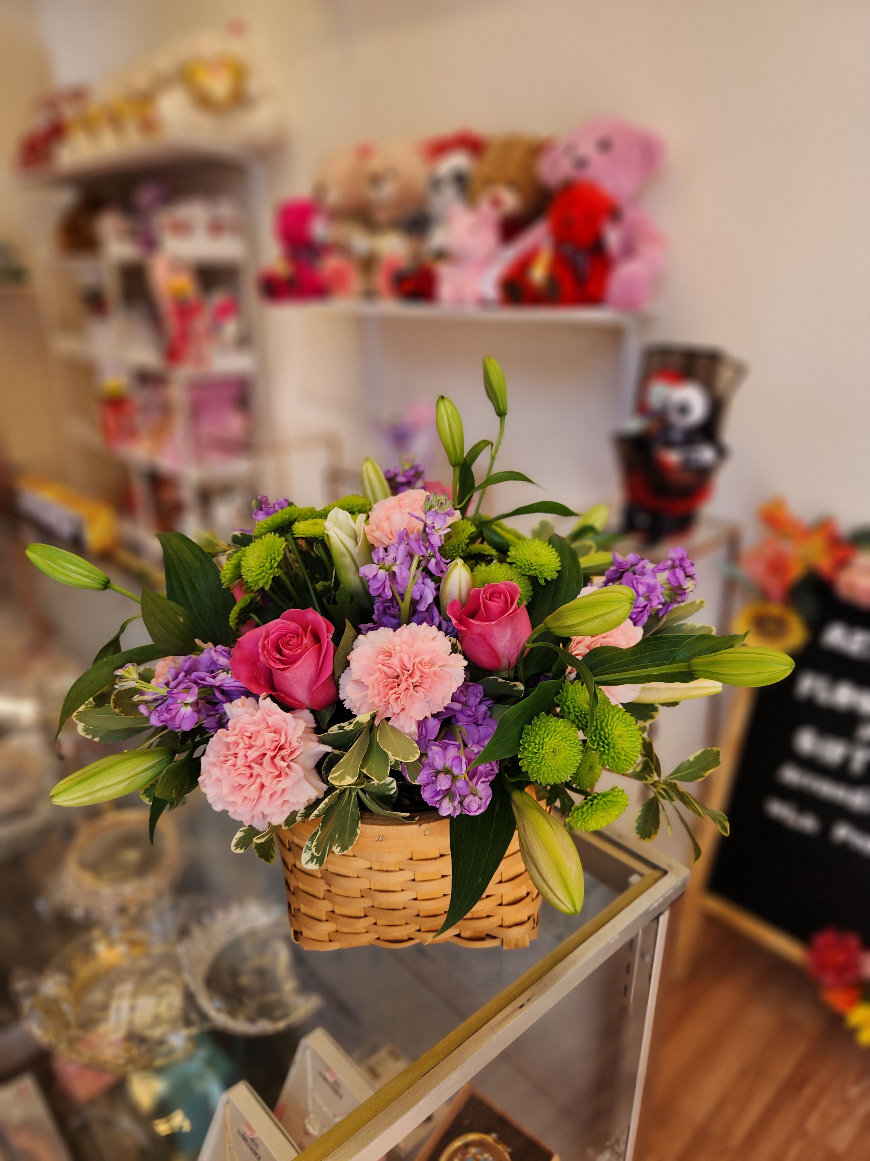 Basket arrangement of pink roses, carnations, lilies, and purple flowers