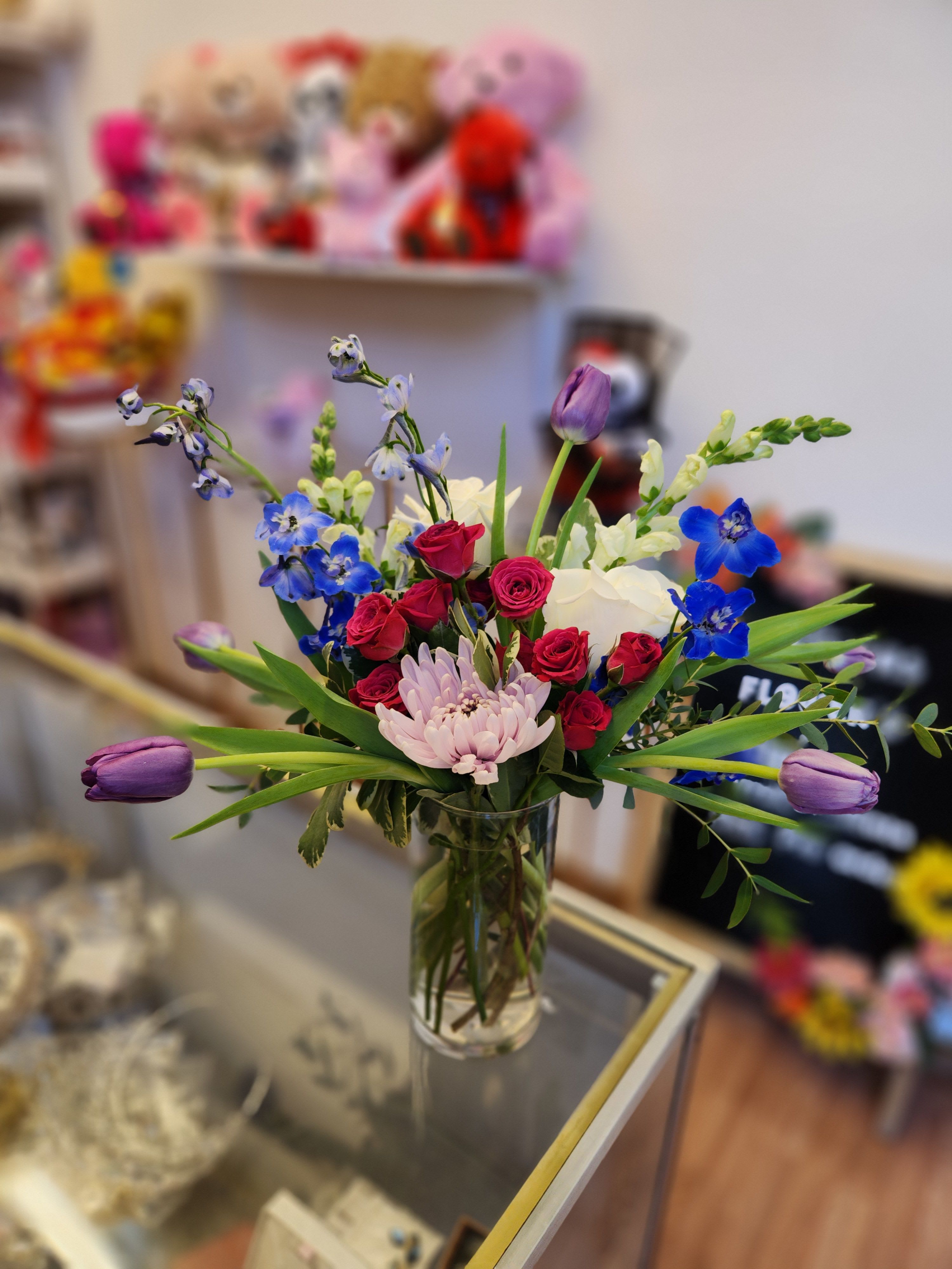 Mixed bouquet of roses, tulips, and blue flowers in a glass vase