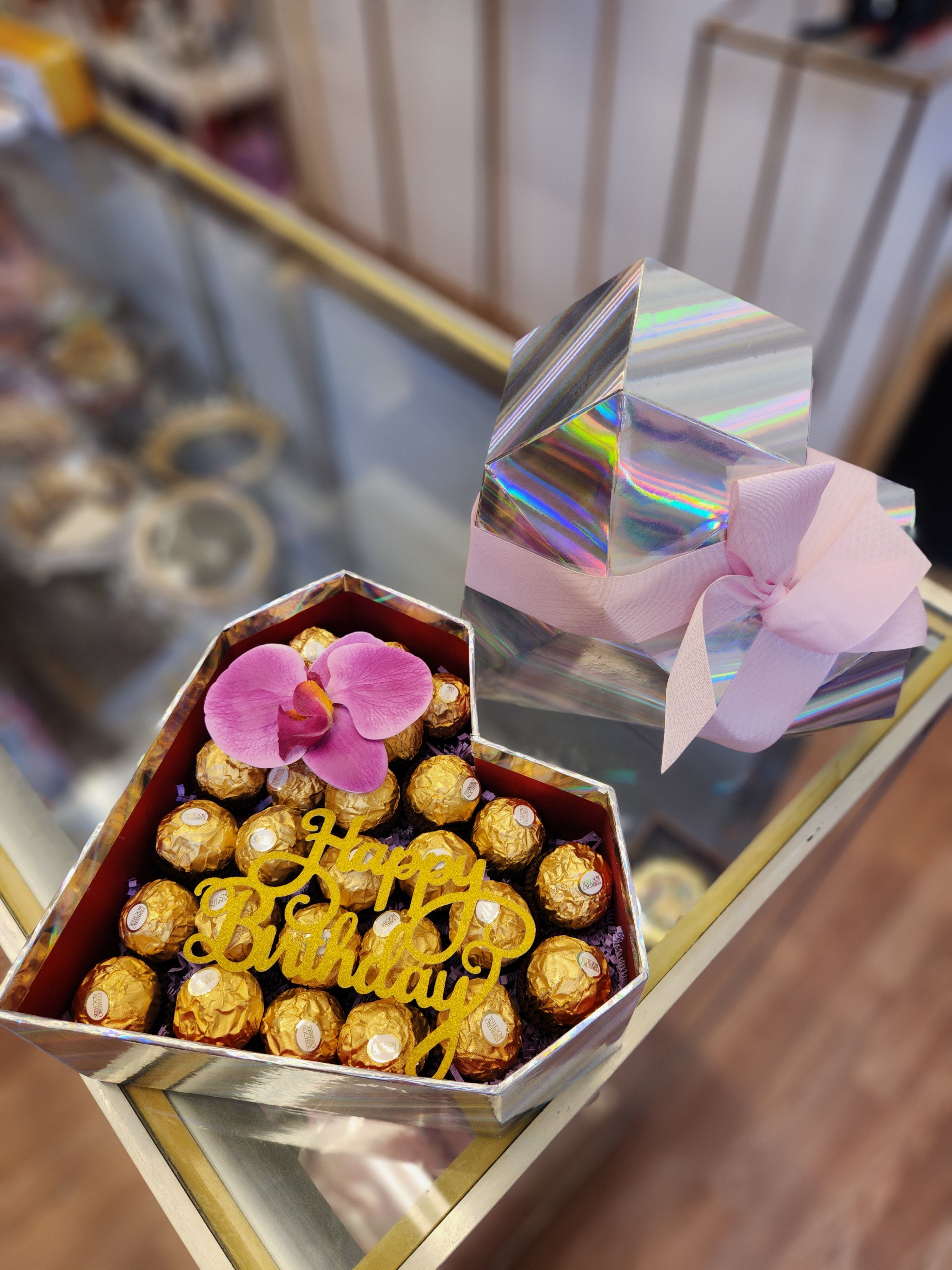 Gift box of chocolates topped with a pink orchid and birthday sign