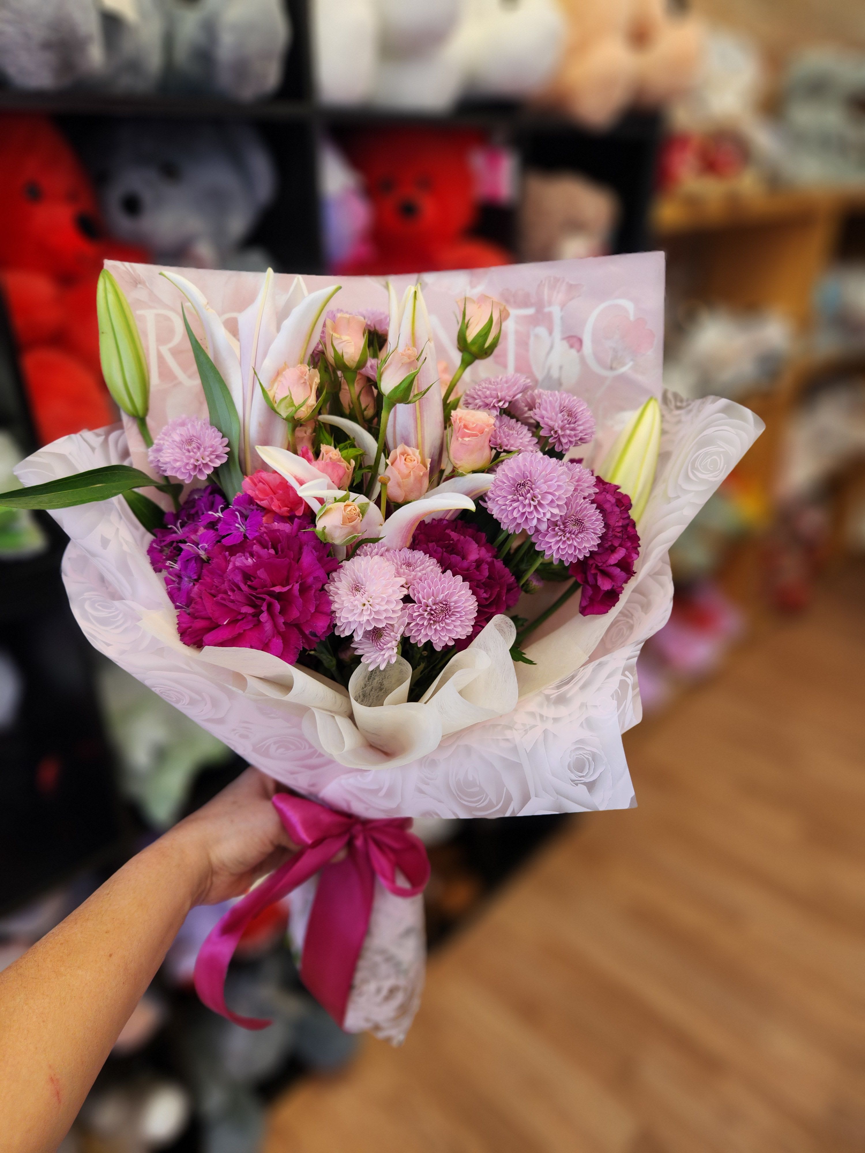Handheld bouquet of pink and white flowers wrapped in pale paper