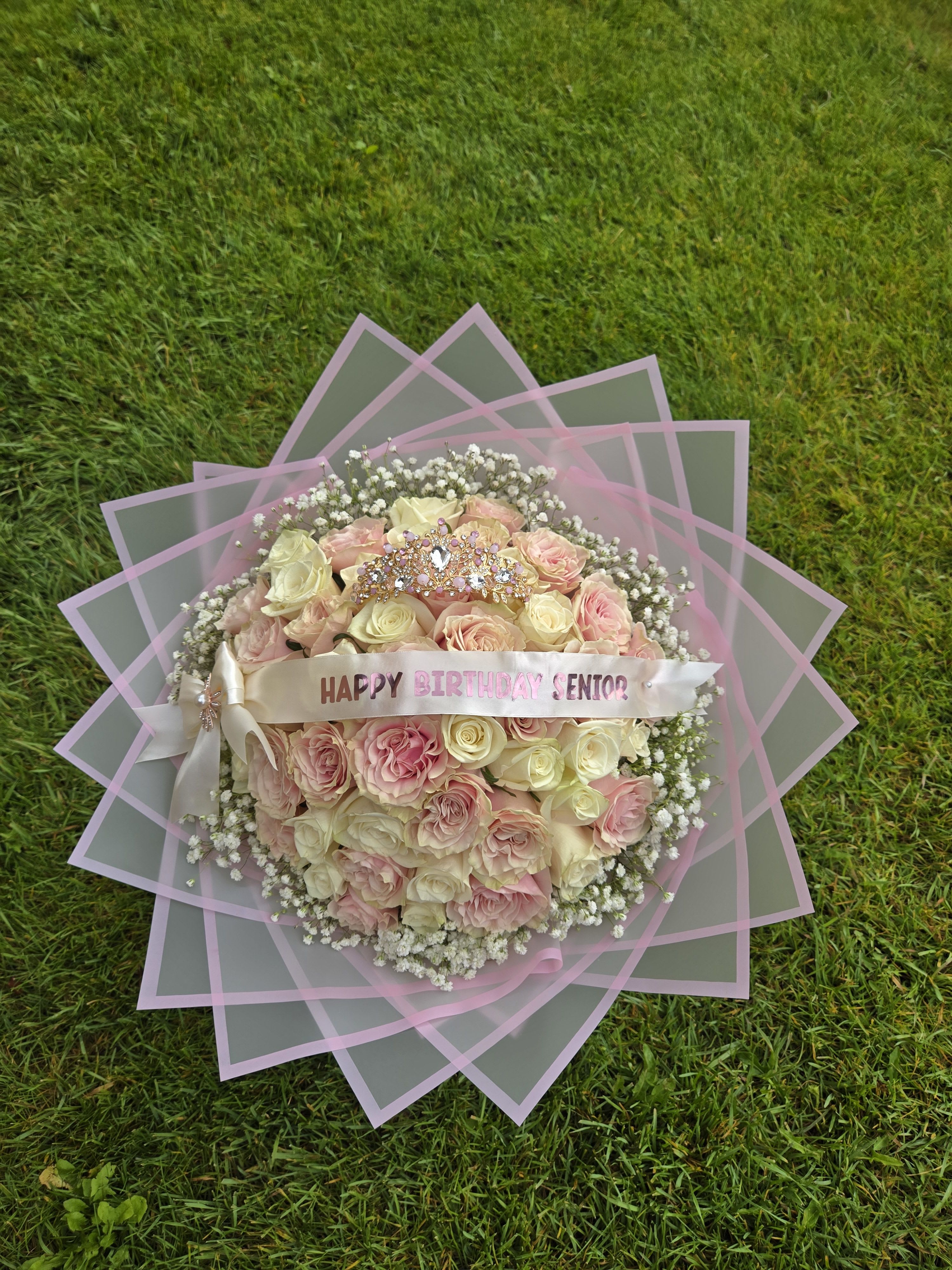 Pink and cream rose bouquet with a birthday ribbon on grass