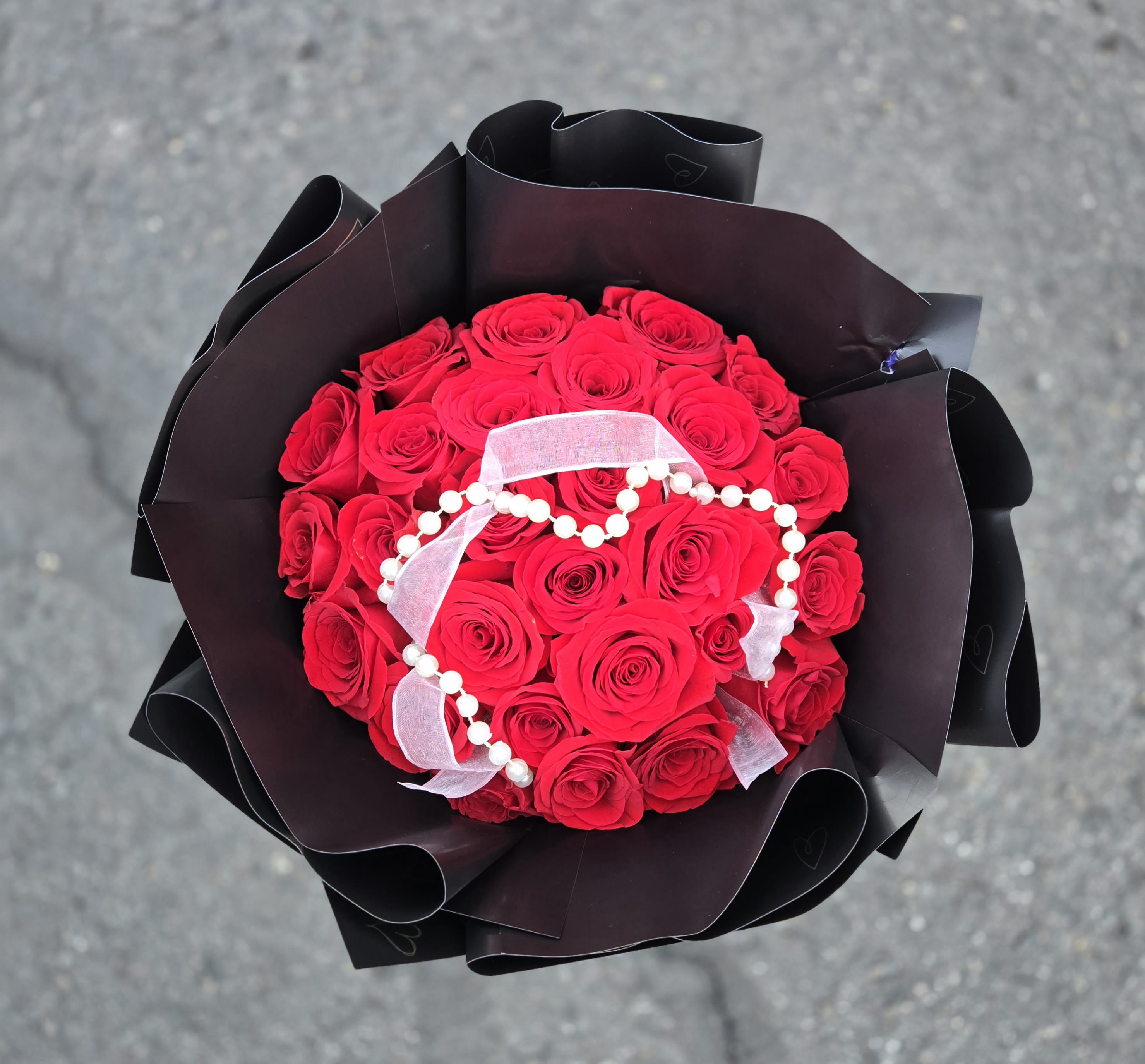 Bouquet of red roses wrapped in black paper with a white ribbon
