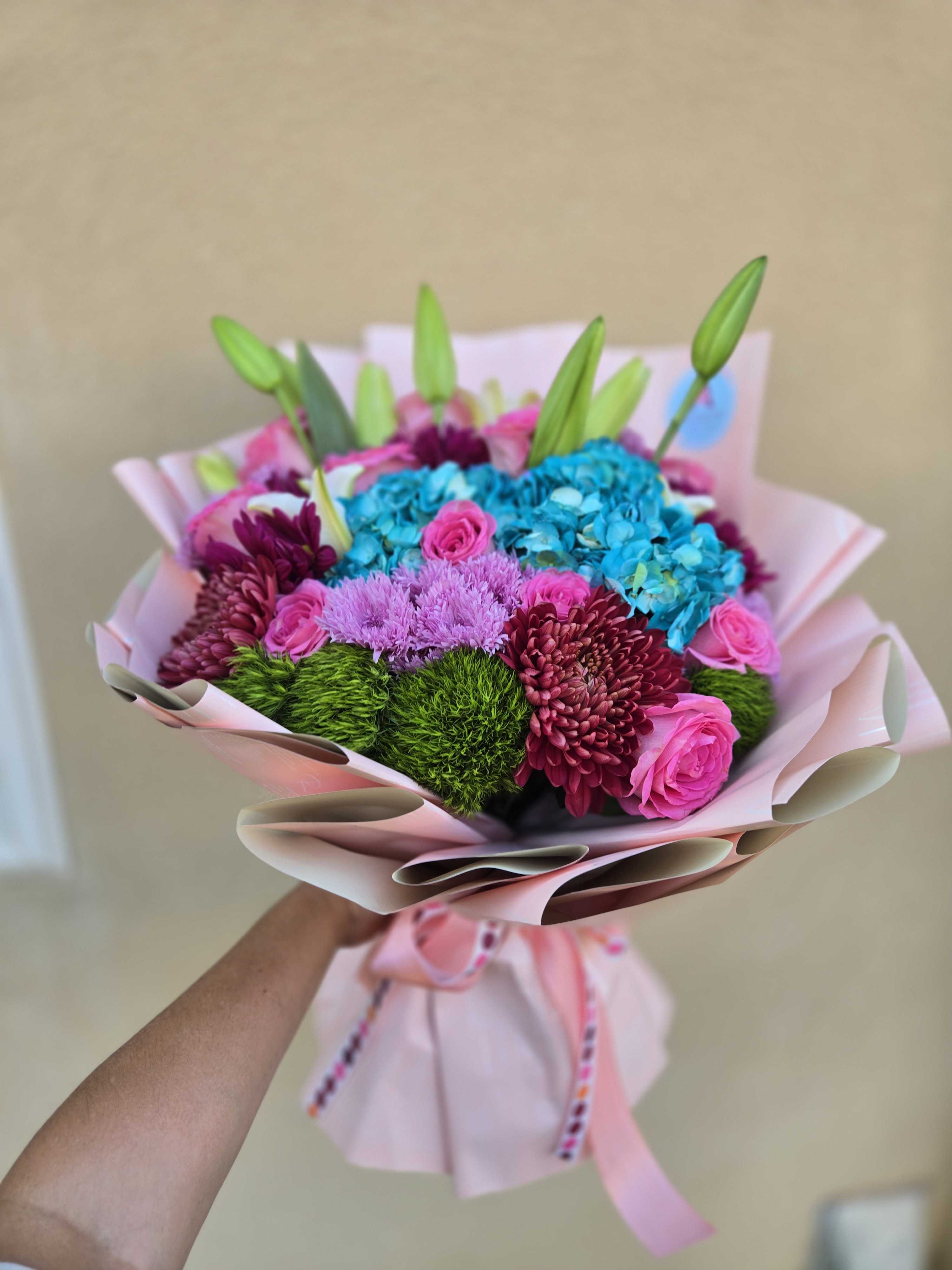 Bouquet of pink roses, blue hydrangeas, and purple chrysanthemums wrapped in pink paper