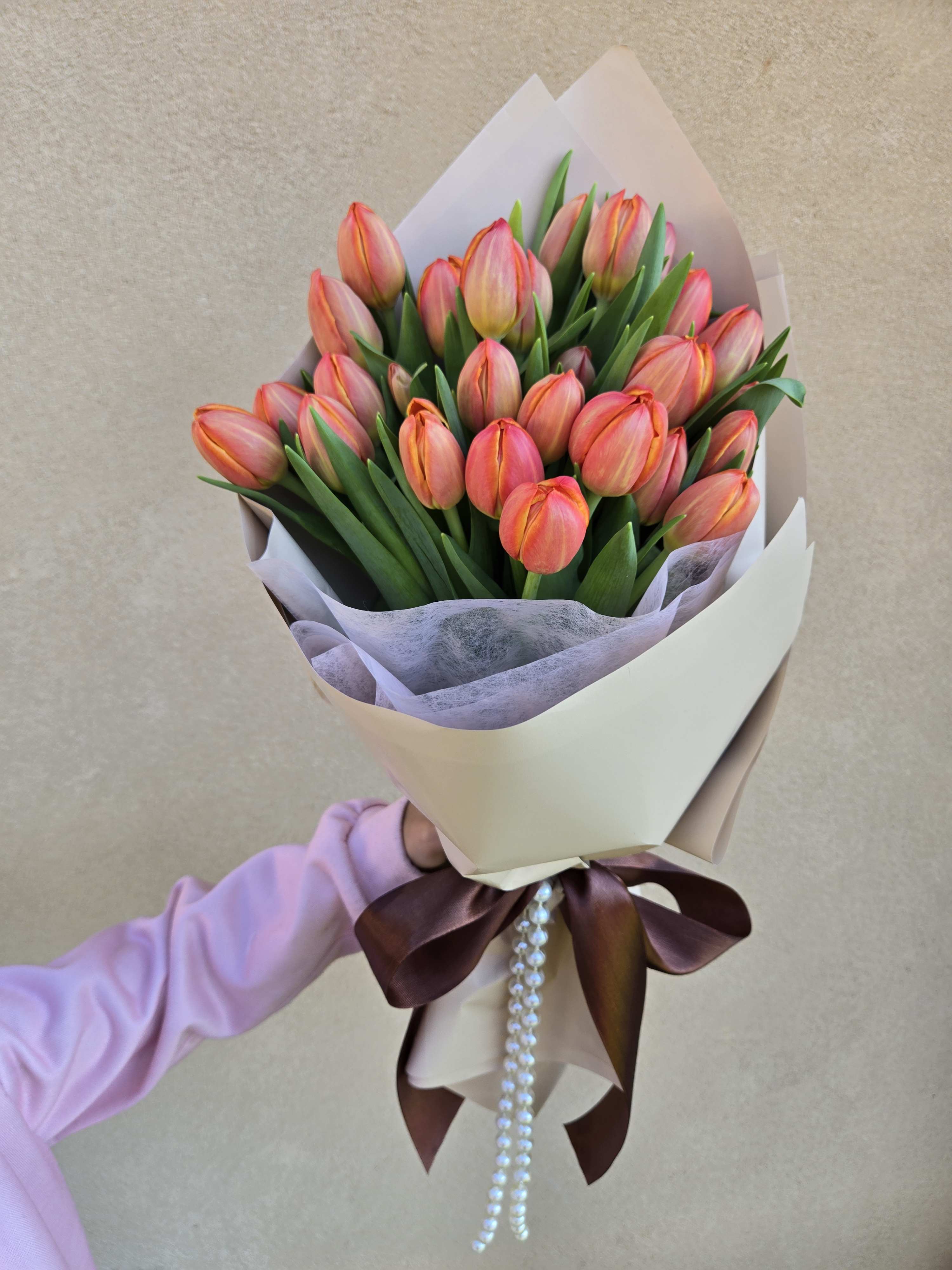 Bouquet of pink-orange tulips wrapped in cream paper with a ribbon