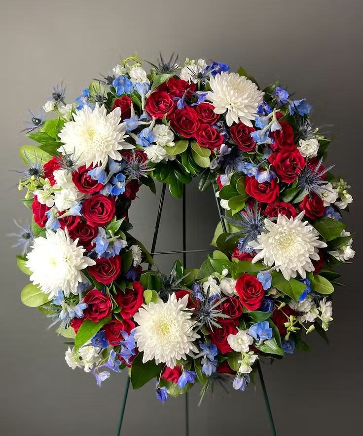 Circular wreath of red roses, white chrysanthemums, and blue flowers on a stand