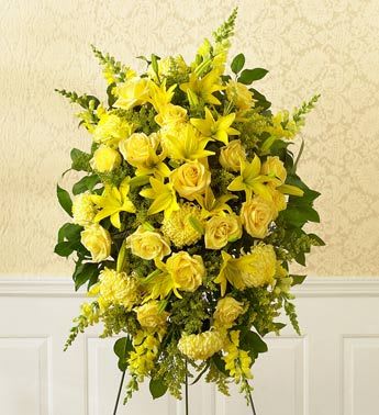 Yellow floral standing spray with roses and lilies on a black easel