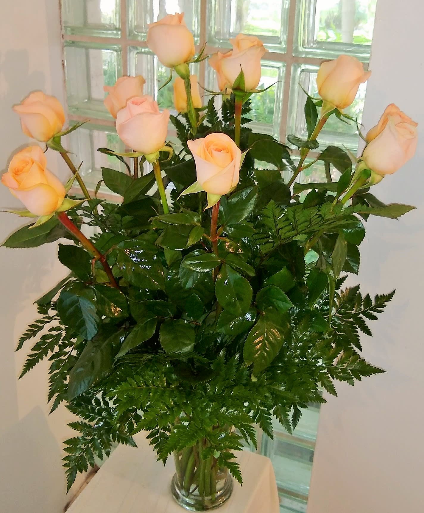 Peach roses arranged in a clear glass vase with fern foliage