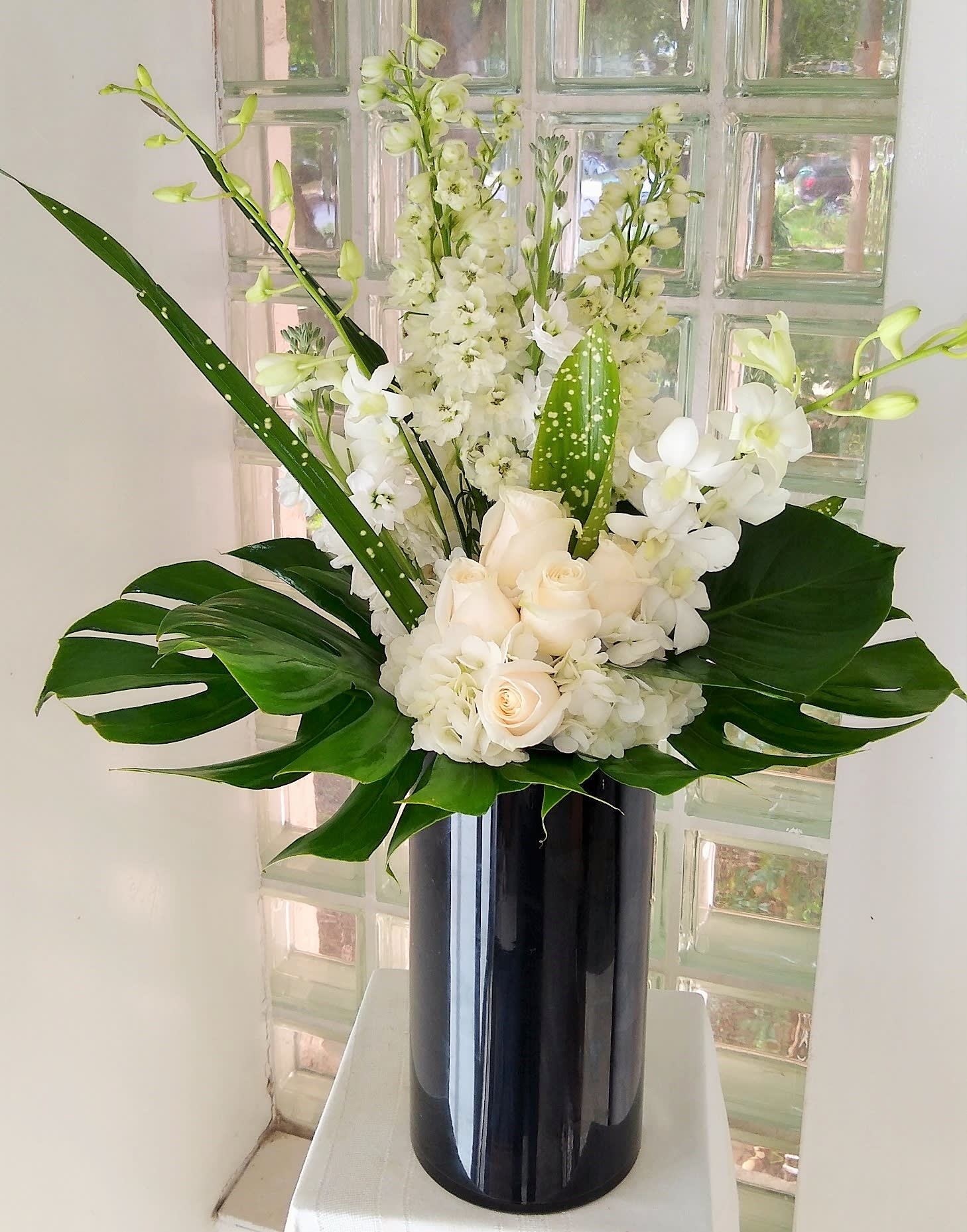 White floral arrangement in a tall black vase with large green leaves