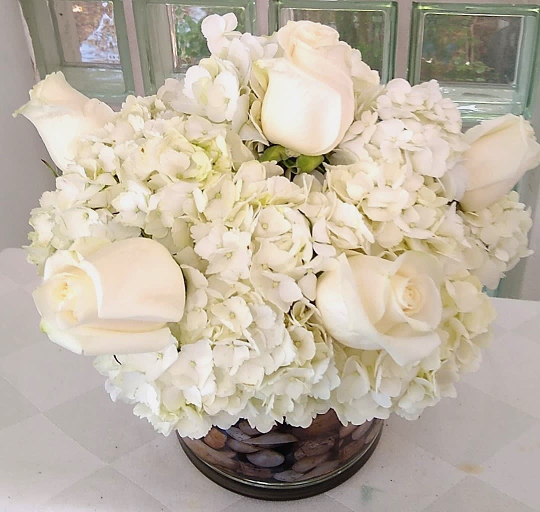 White roses and hydrangeas arranged in a round glass vase