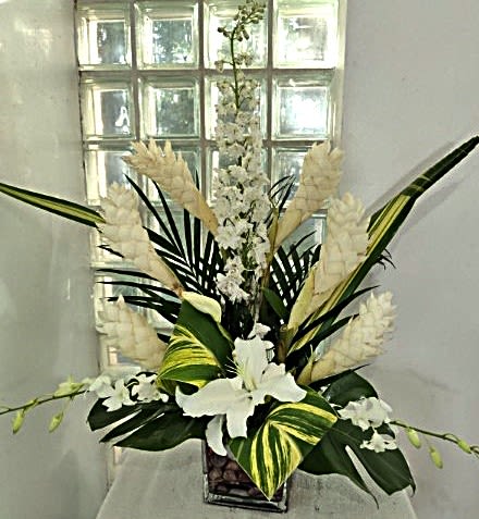 Tall white floral arrangement in a square vase with large tropical leaves