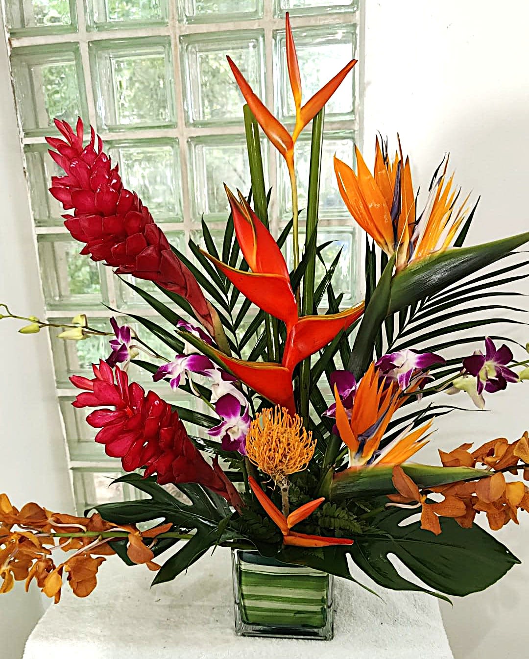 Tropical flower arrangement with orange bird-of-paradise and red ginger in a glass vase