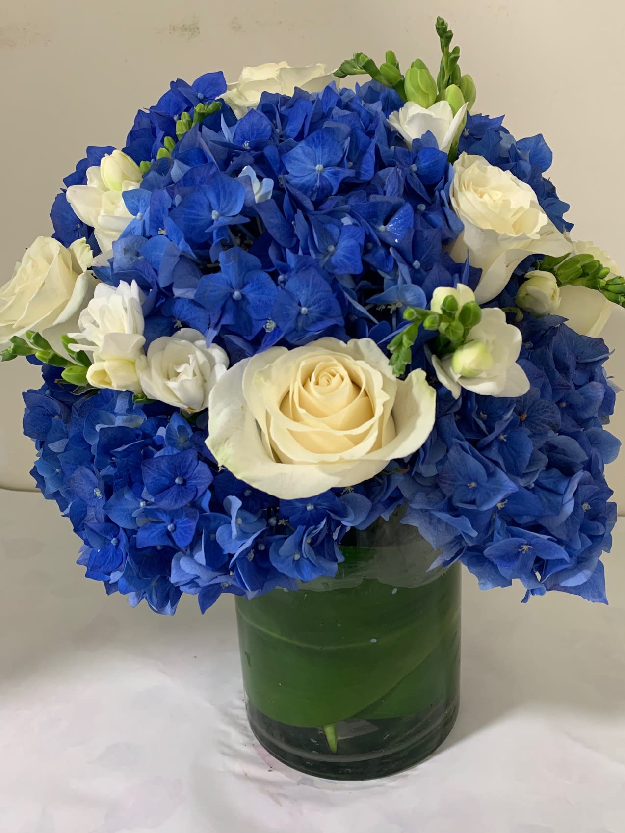 Blue Dutch Supreme &amp; Roses - Beautiful arrangement, made with the finest Blue Dutch Hydrangea and White Roses, Standing about 16 inches tall and 12-14 inches Wide. Arranged in a 8 inch tall glass vase with a 5 inch opening and wrapped elegantly with a leaf