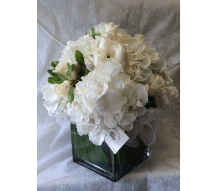 Sagaponack  Beach - by Dutch Petals - The photo does not do this justice this is a large arrangement of the finest Hydrangea from Holland together with White Roses and greens to compliment and is simply stunning.  - Arranged in a 7 inch glass cube wrapped with a leaf inside. a stunning gift or simply place in the center of any table.  - people will be talking about arrangement. Stands about 18 inches tall and around is about 15 inches all sides. Available for local delivery only