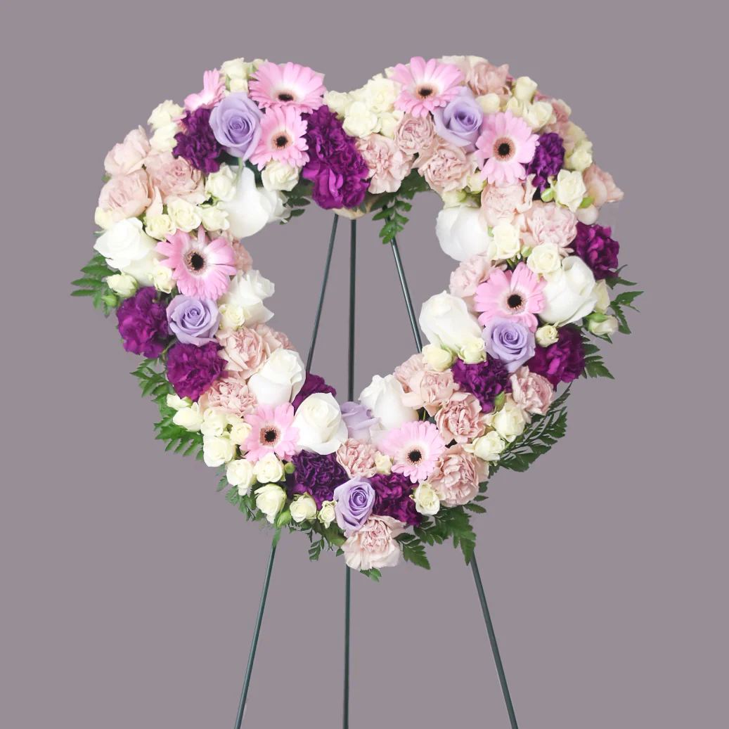 Heart-shaped floral wreath on a stand with pink, white, purple flowers