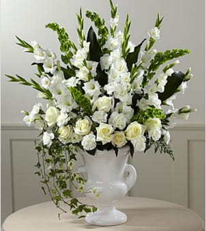 White floral arrangement in a white urn vase with trailing greenery