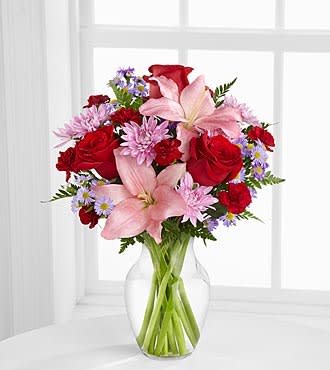 Bouquet of red roses, pink lilies, and purple daisies in a clear glass vase
