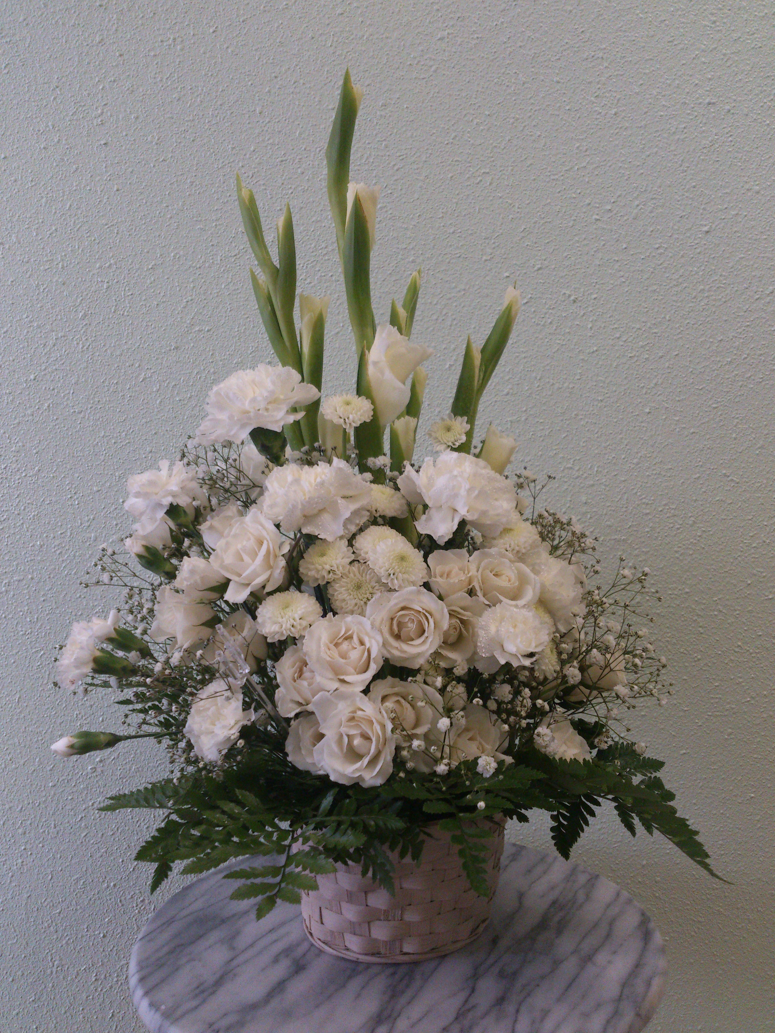White floral arrangement in a woven basket with tall green stems