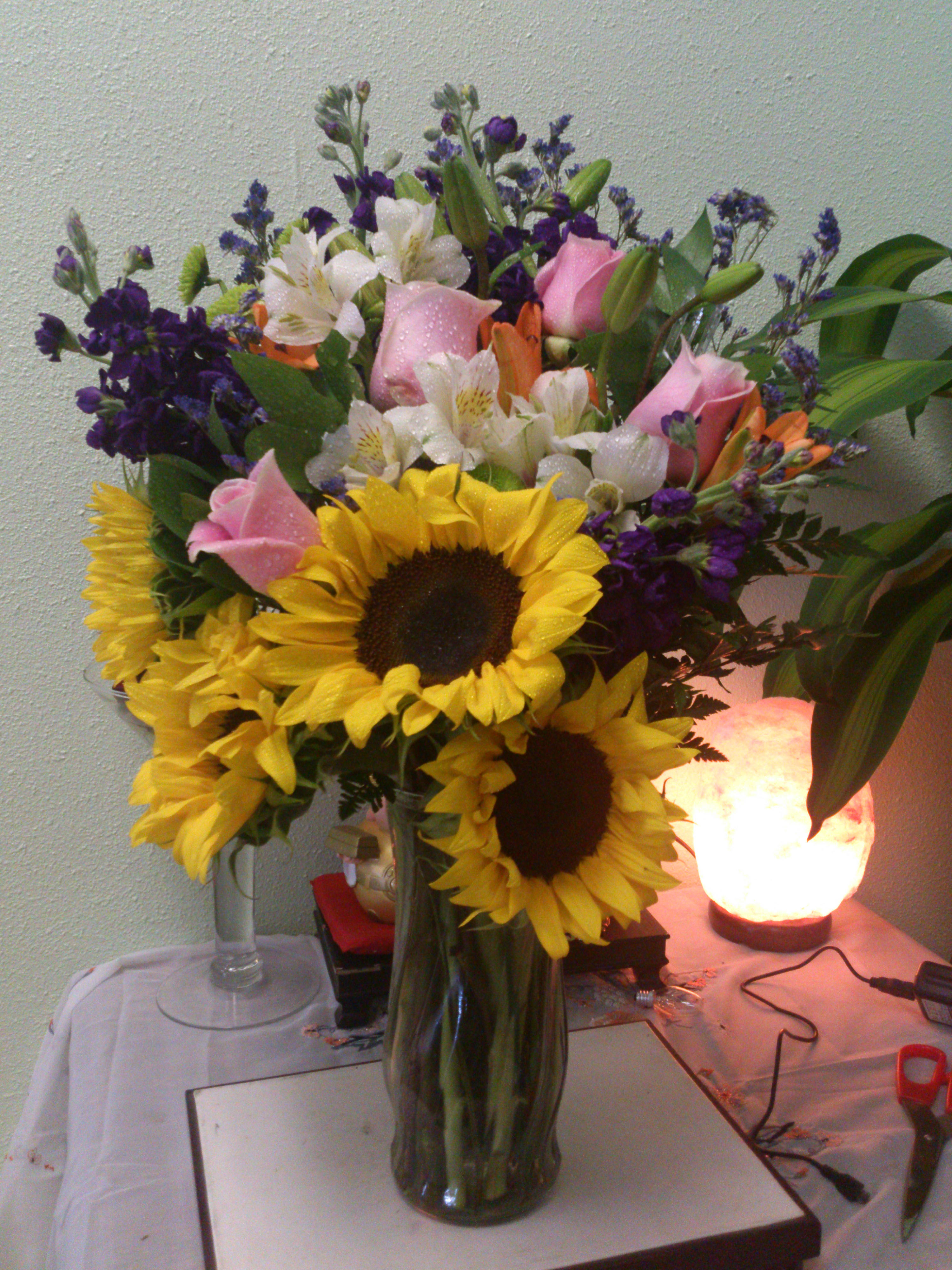 Bouquet of sunflowers, pink roses, and white lilies in a glass vase