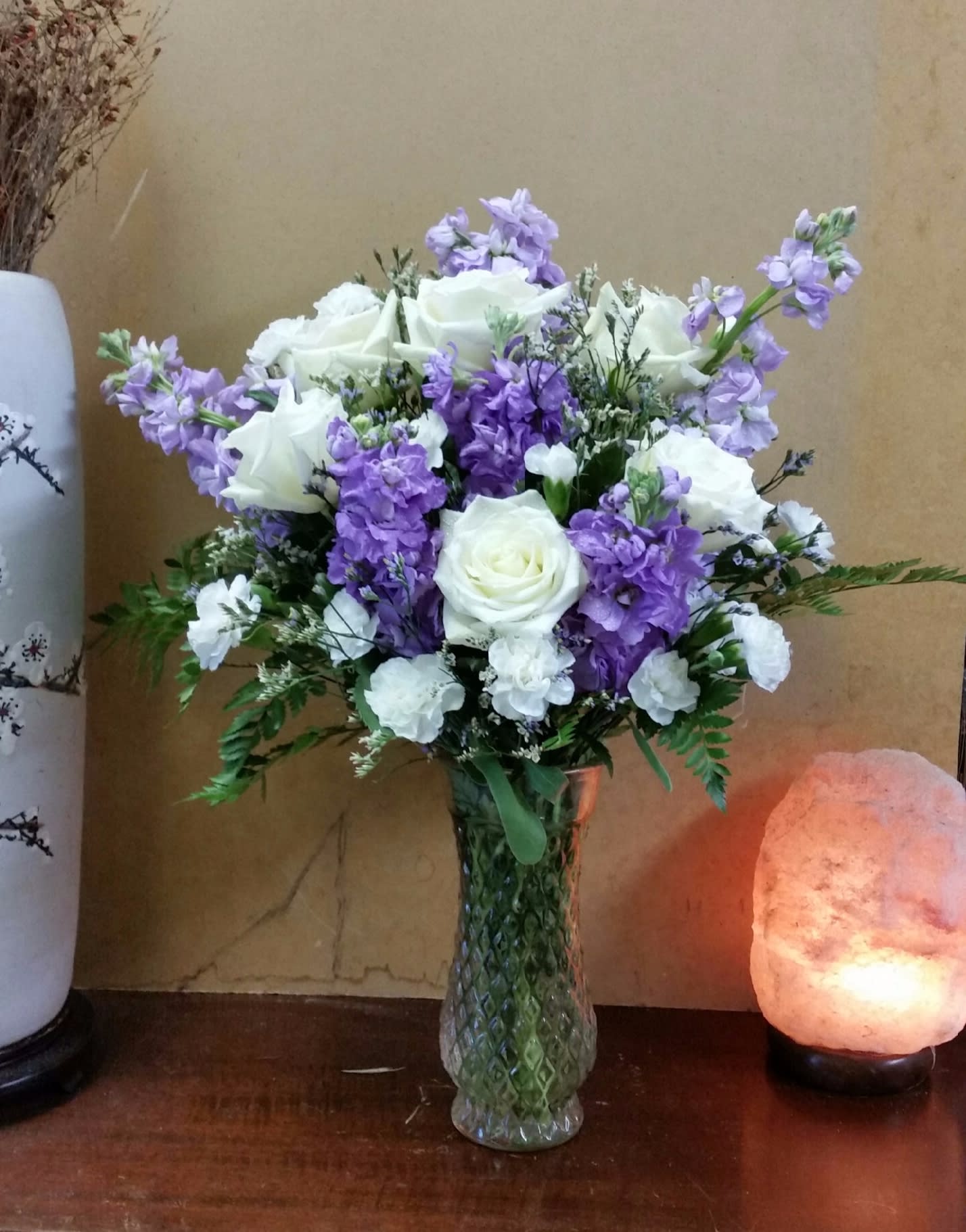 White roses and purple flowers arranged in a glass vase