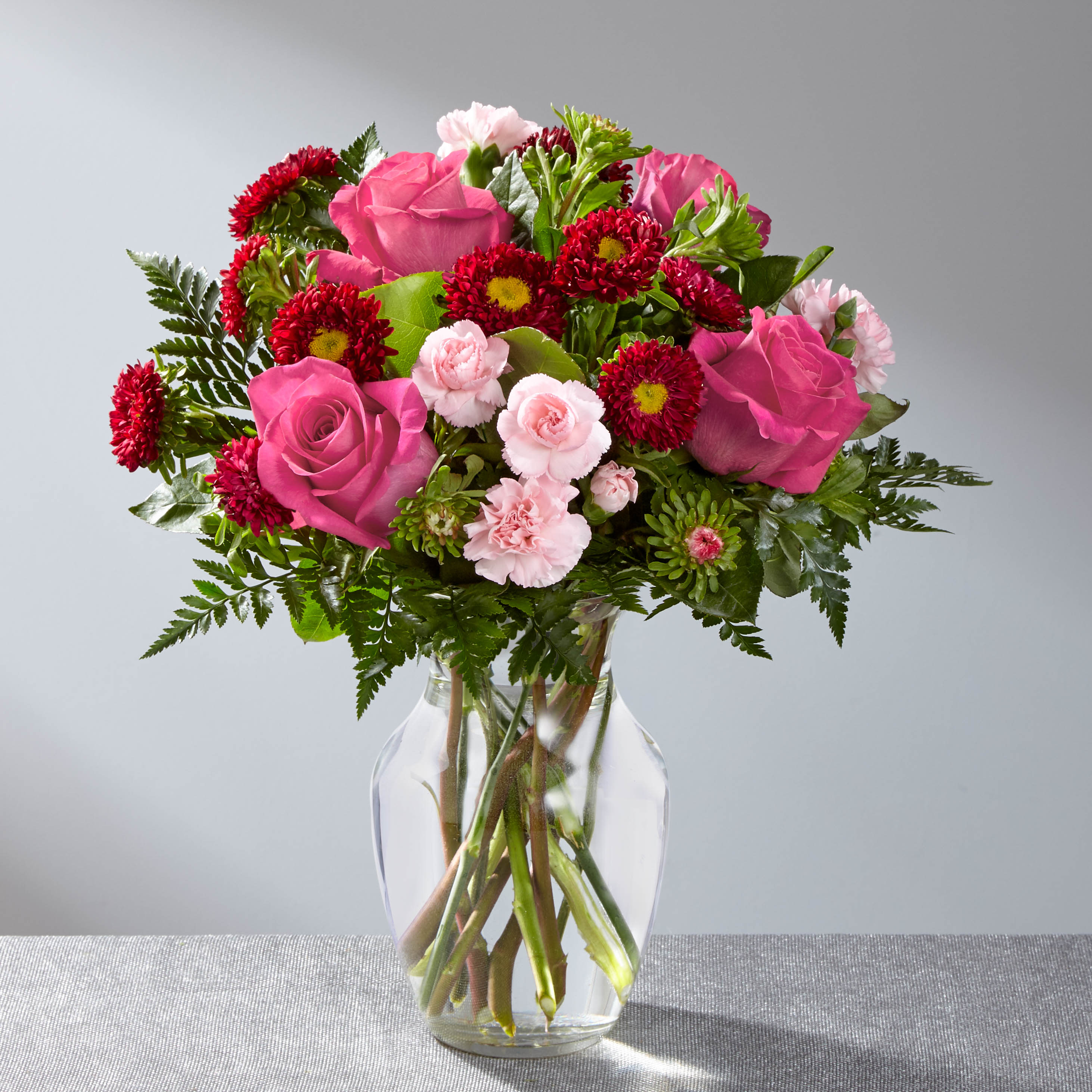 Pink roses and red daisy flowers arranged in a clear glass vase.