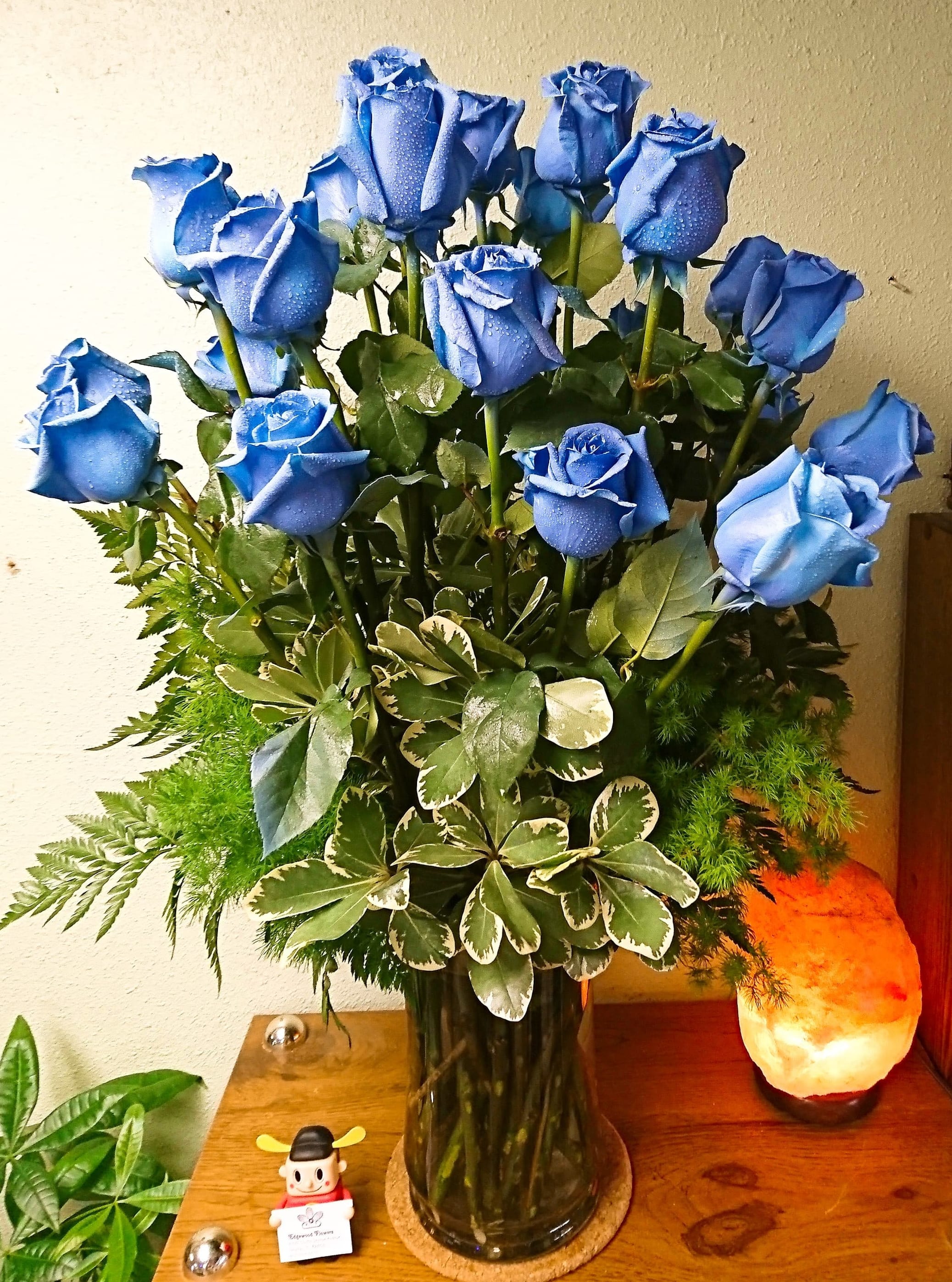 Blue roses arranged in a glass vase with mixed greenery