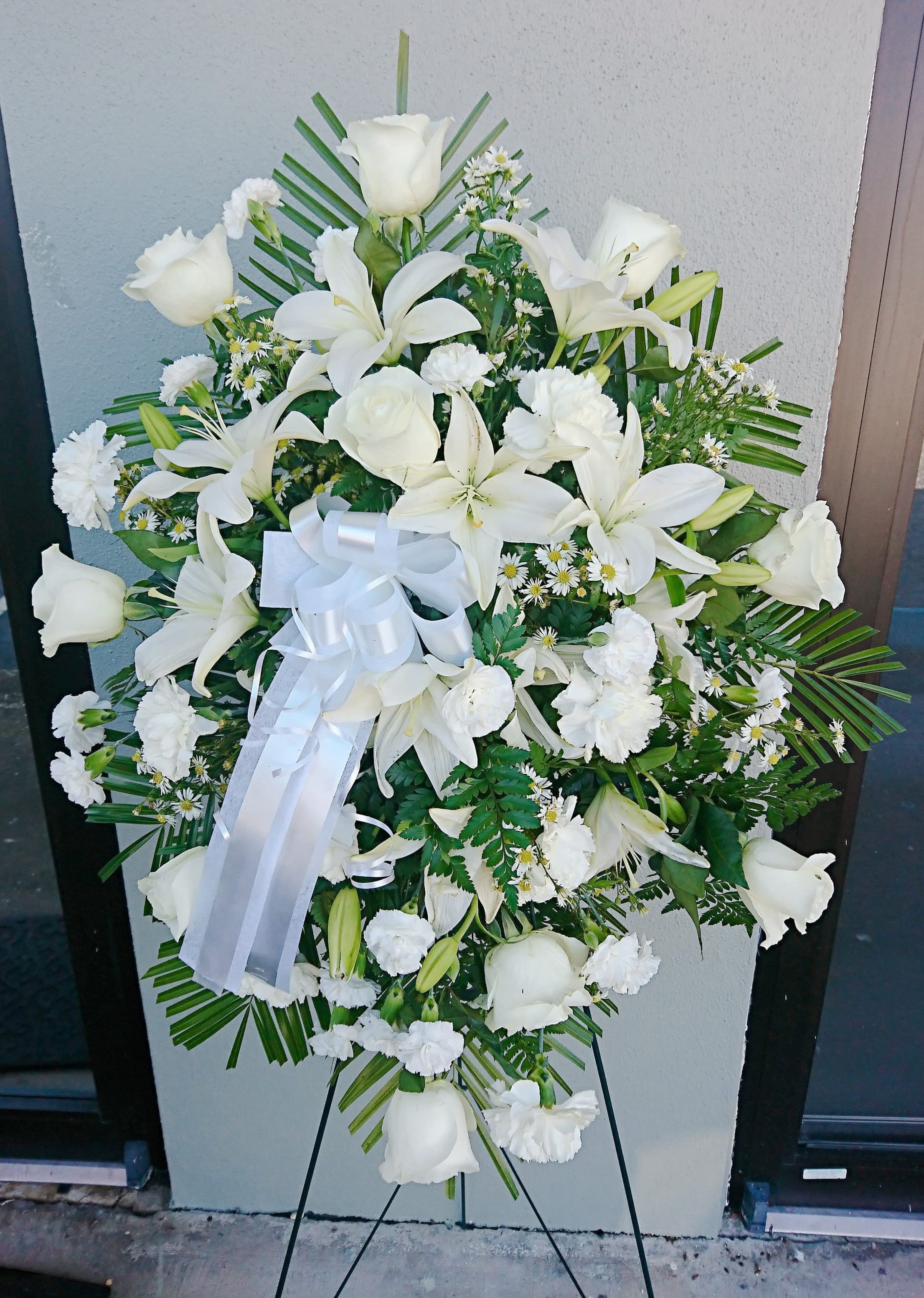 White funeral spray with lilies, roses, and carnations on an easel